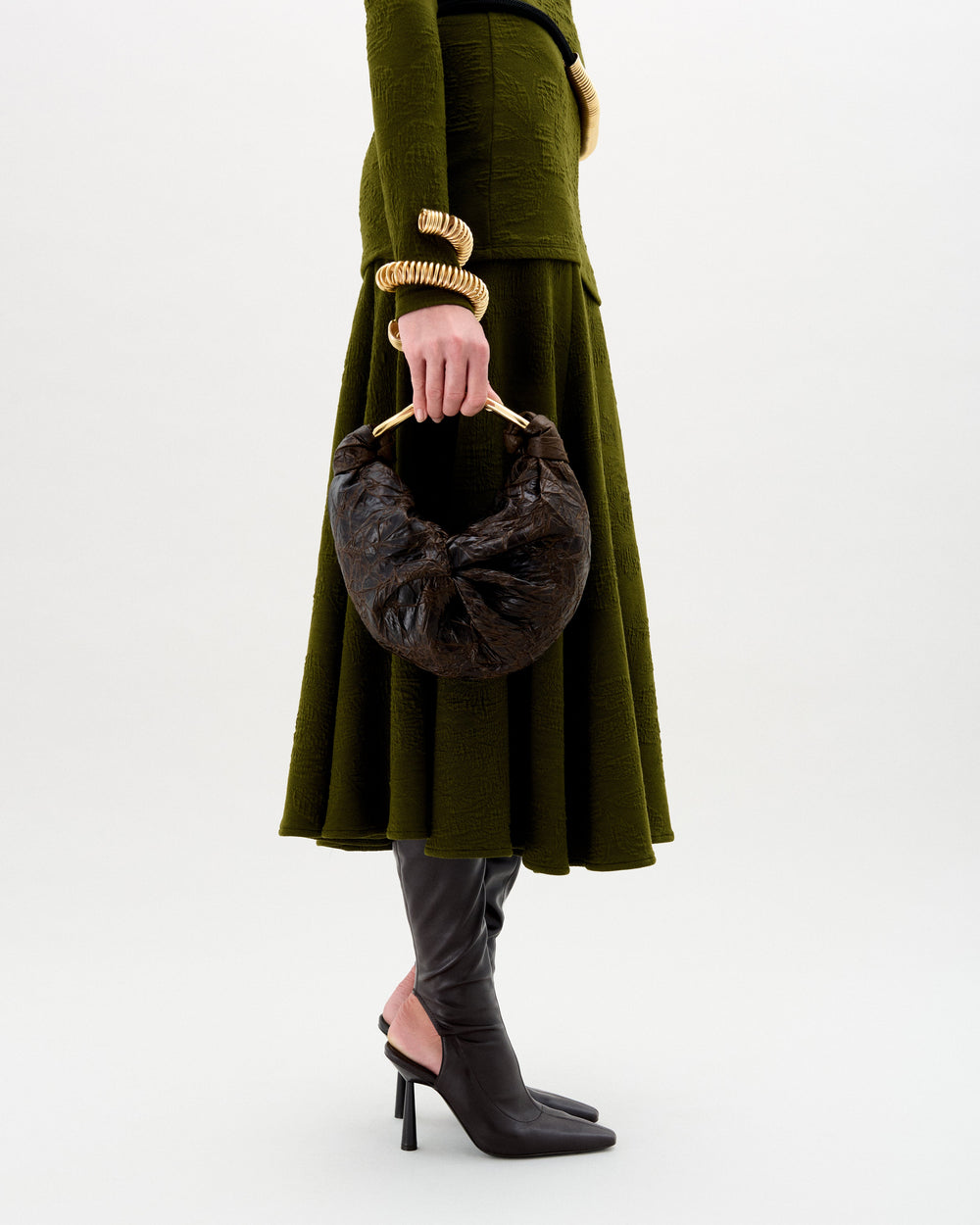 Person wearing a green coat holding a brown handbag on a white background
