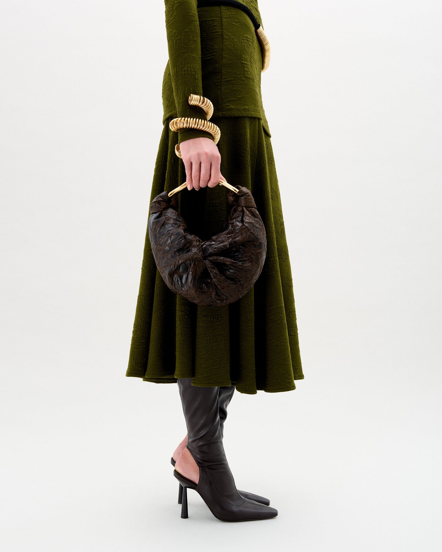Person wearing a green coat holding a brown handbag on a white background
