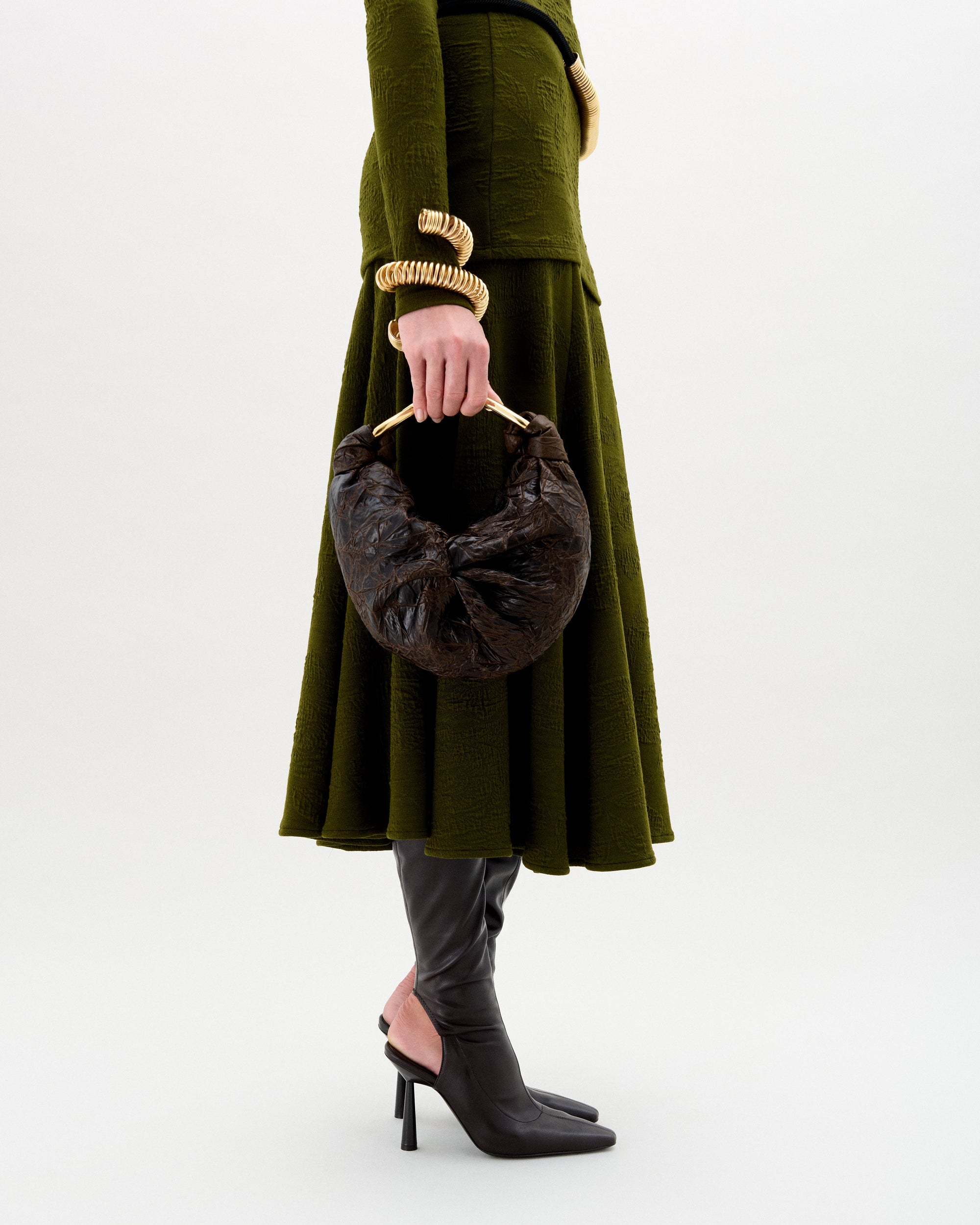 Person wearing a green coat holding a brown handbag on a white background