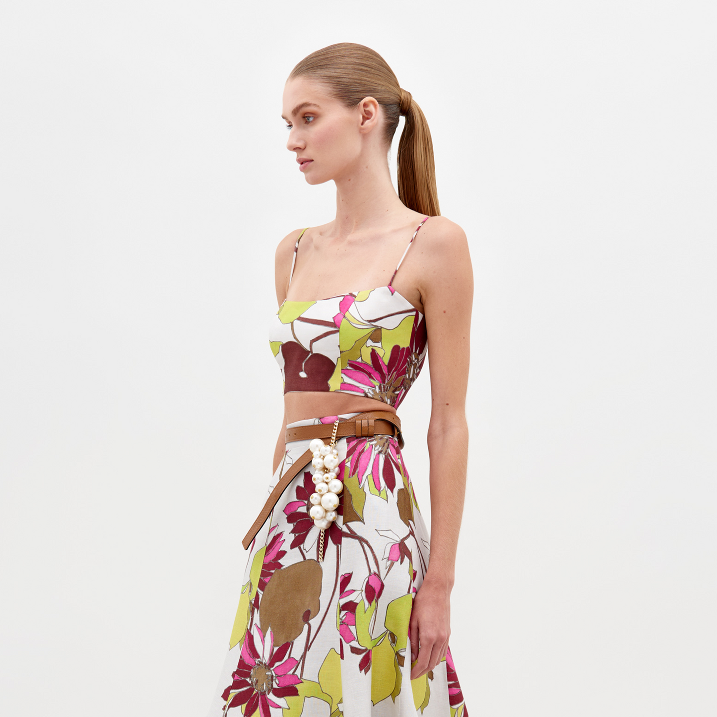 Woman in the Trini Top Botanical Multifloral paired with a pearl-embellished belt, side profile, against a plain white background. Mark your calendars: Orders placed by February 15th, 2025 will meet the guaranteed ship by date.