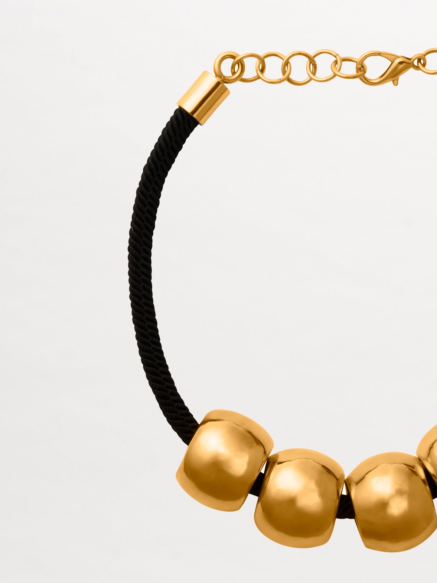 The Tristana Necklace is a black 3D cord choker featuring four large round gold beads with intricate details and a secure gold lobster clasp, all beautifully crafted against a plain backdrop. Made in Colombia.