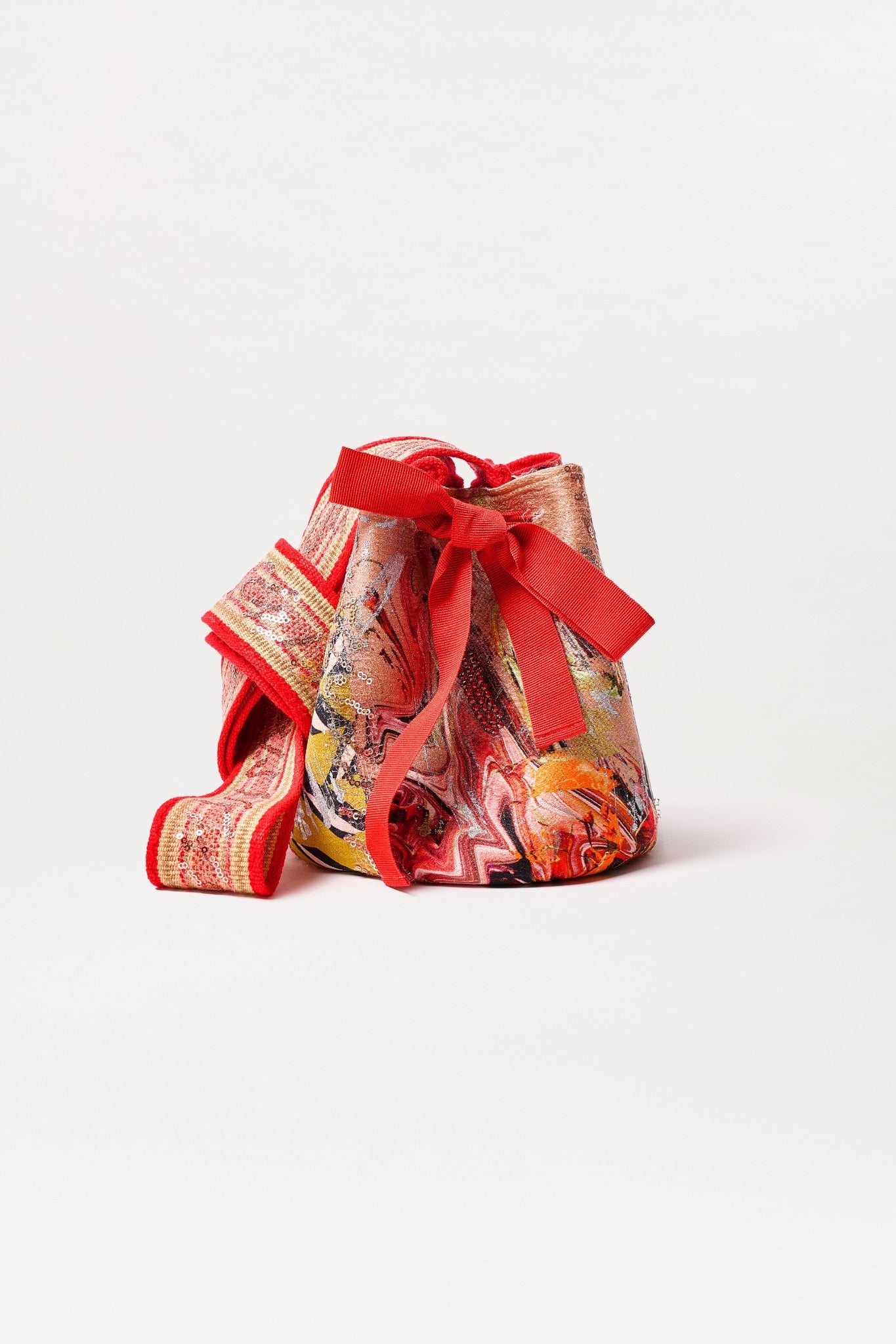 The Mochila Laaput Small is a colorful Colombian bag with a vibrant abstract pattern, red ribbon drawstring, decorative bow, and a wide red-and-pink woven strap, shown against a plain white background.