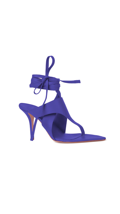 A vibrant violet Italian leather high-heeled shoe with a pointy toe and long straps for tying around the ankle, isolated on a white background.