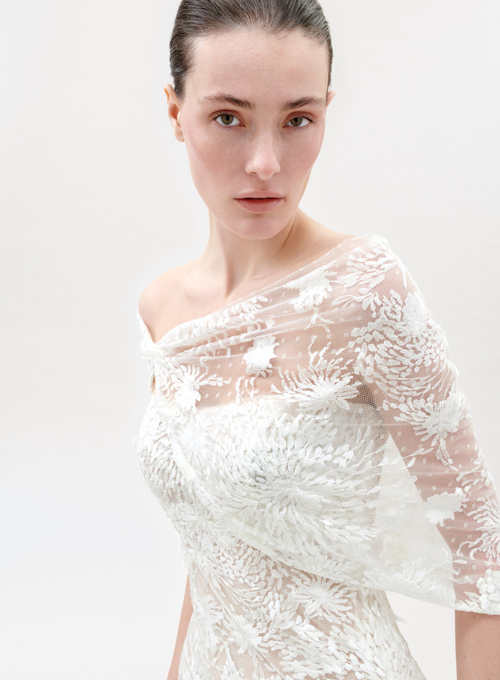 Woman wearing a sheer white lace dress against a plain background