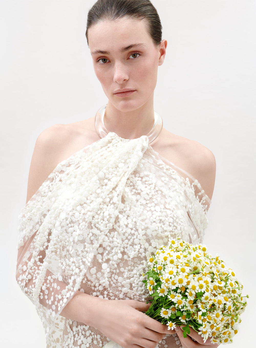 Woman in a white lace dress holding a bouquet of flowers against a plain background