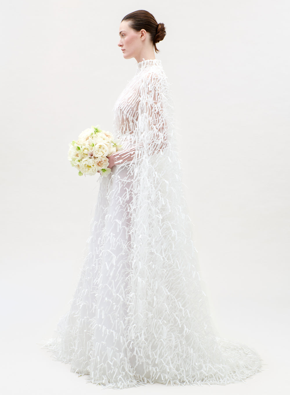 Woman in a white lace wedding dress holding a bouquet on a plain background