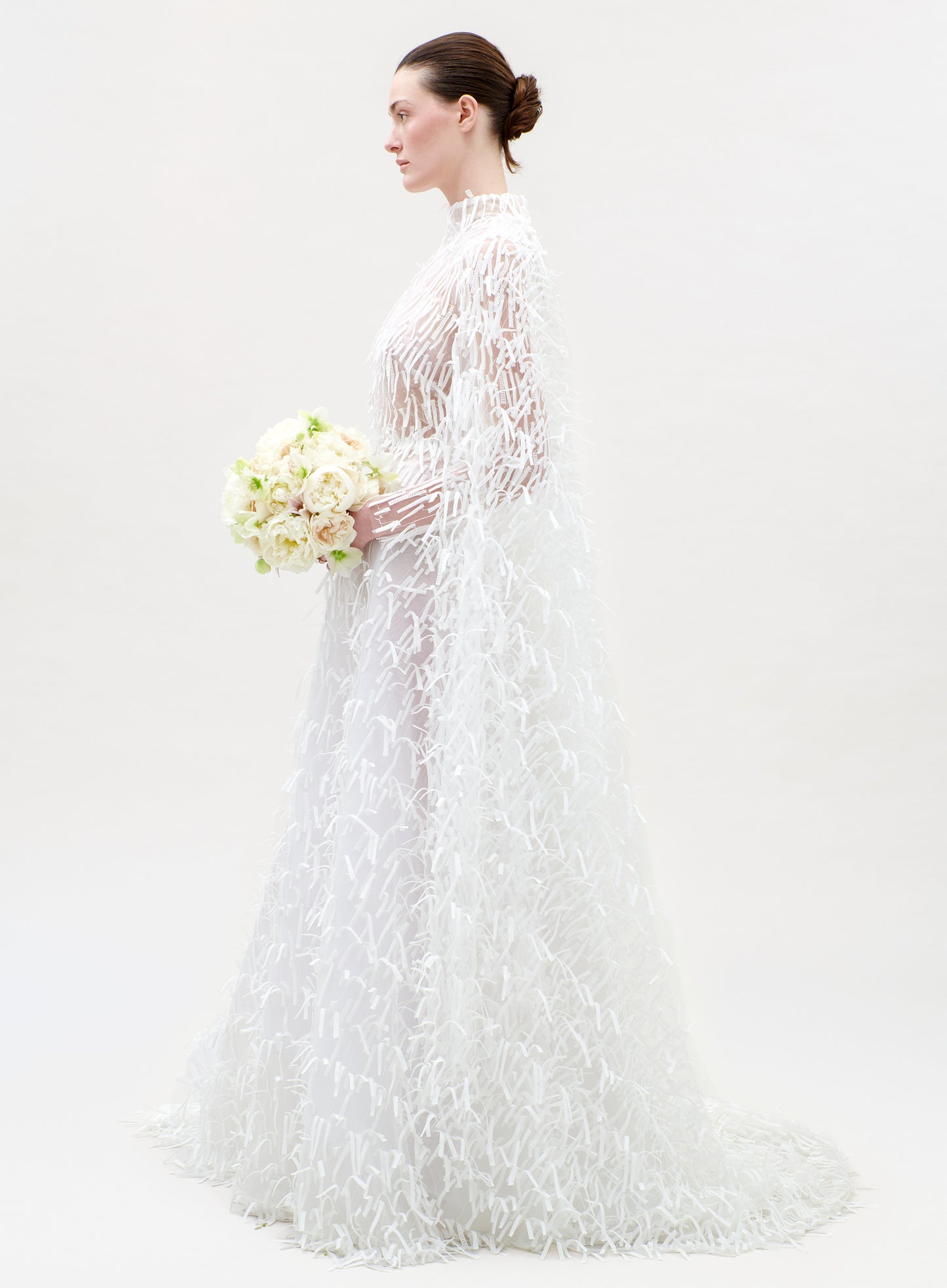 Woman in a white lace wedding dress holding a bouquet on a plain background