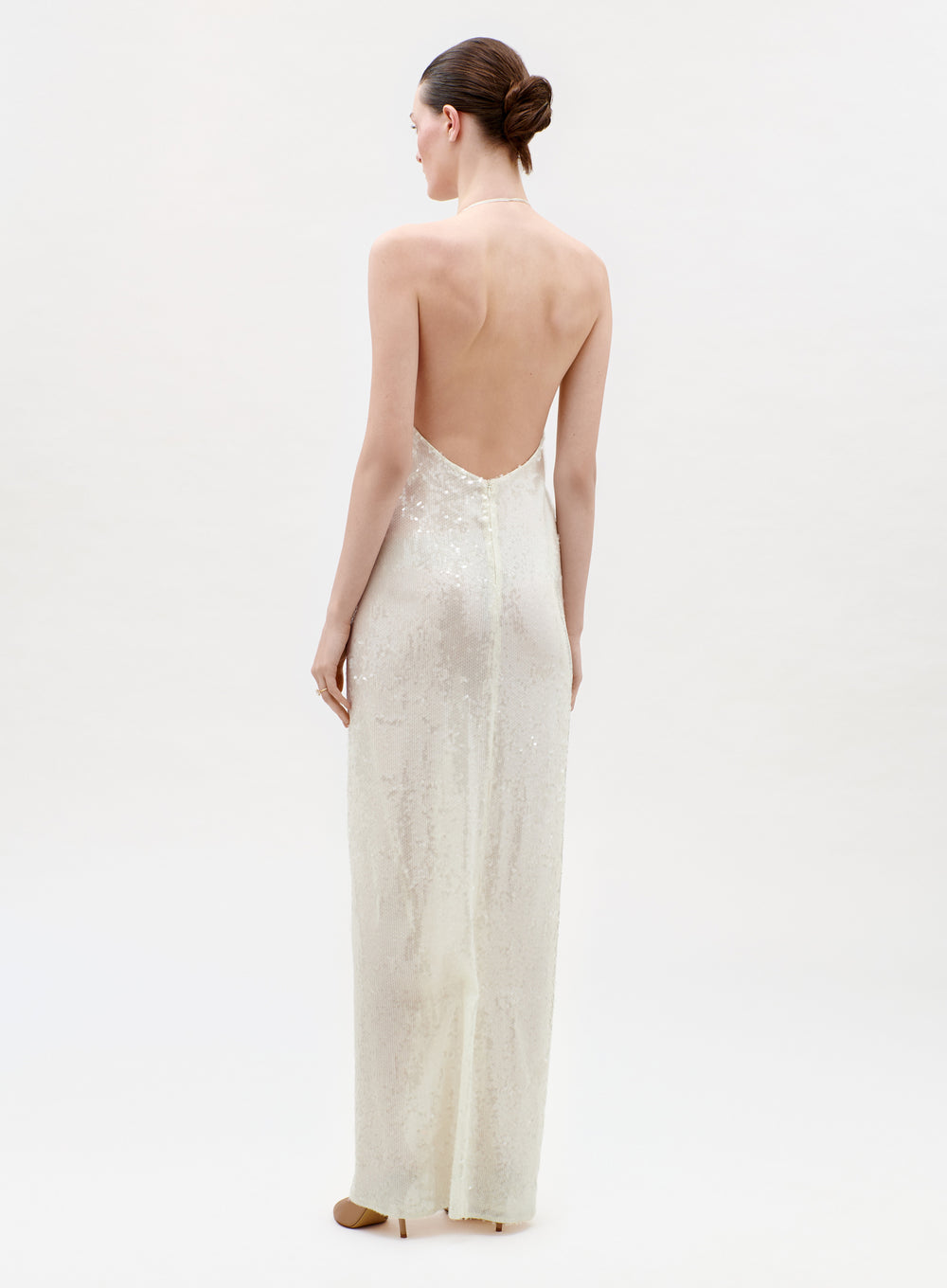 Woman wearing a long, light-colored dress with an open back on a white background