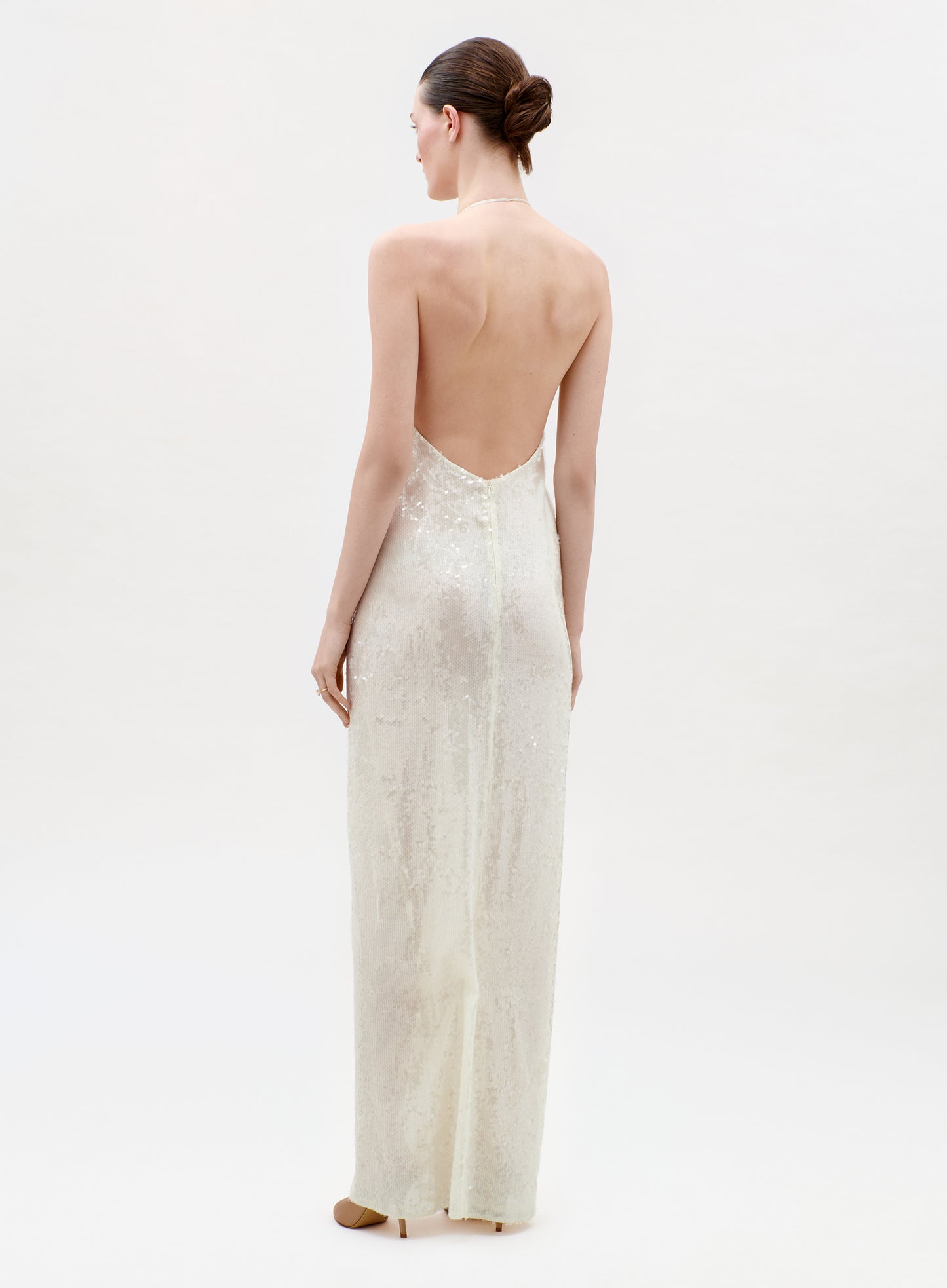 Woman wearing a long, light-colored dress with an open back on a white background