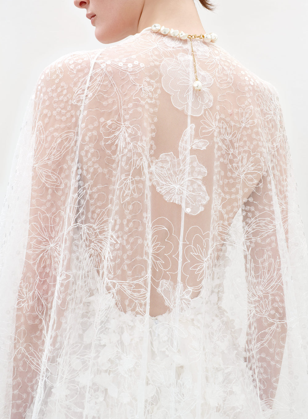 Close-up of a person wearing a sheer lace top with floral patterns on a white background