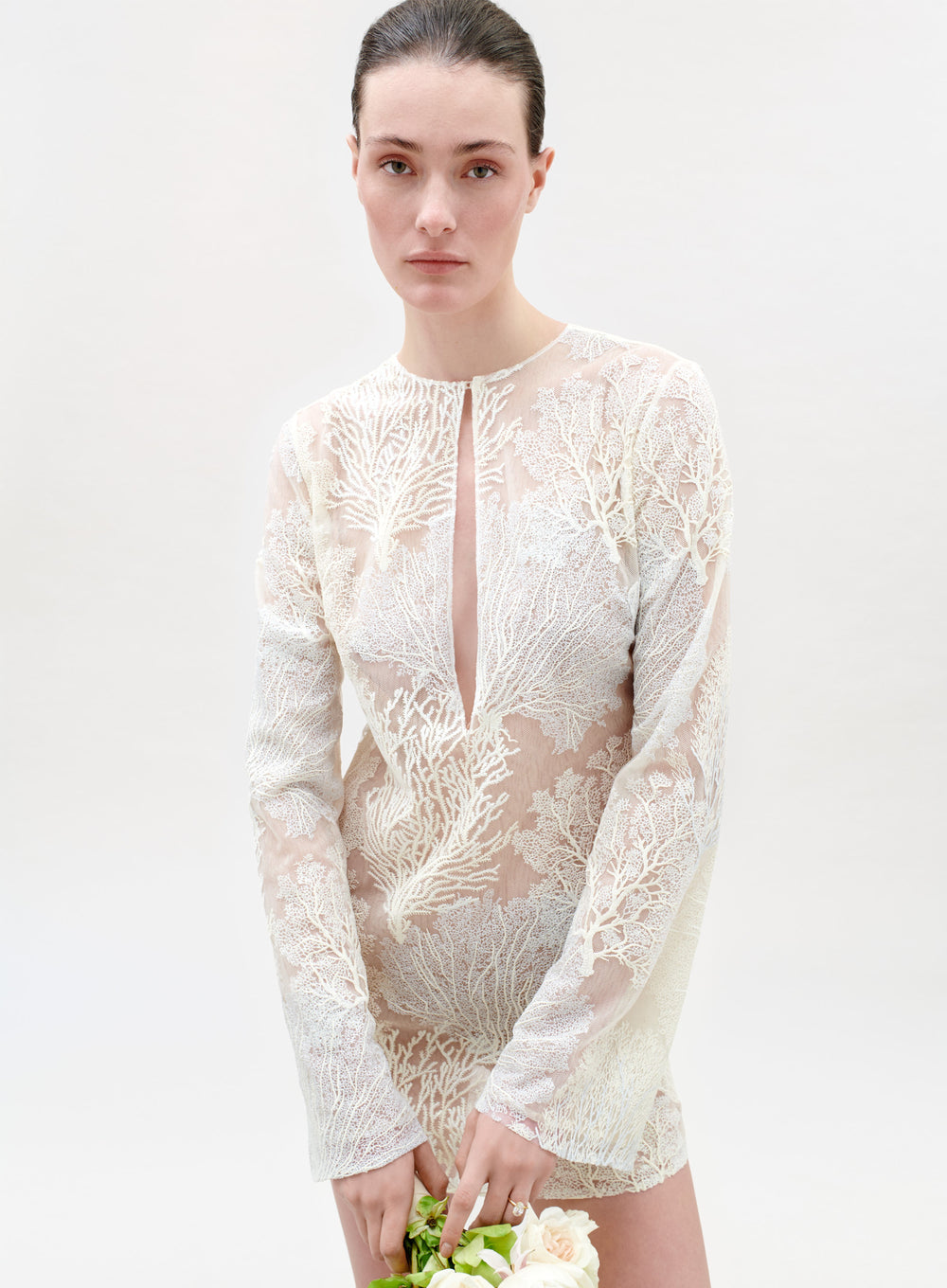 Woman wearing a lace dress holding flowers against a white background