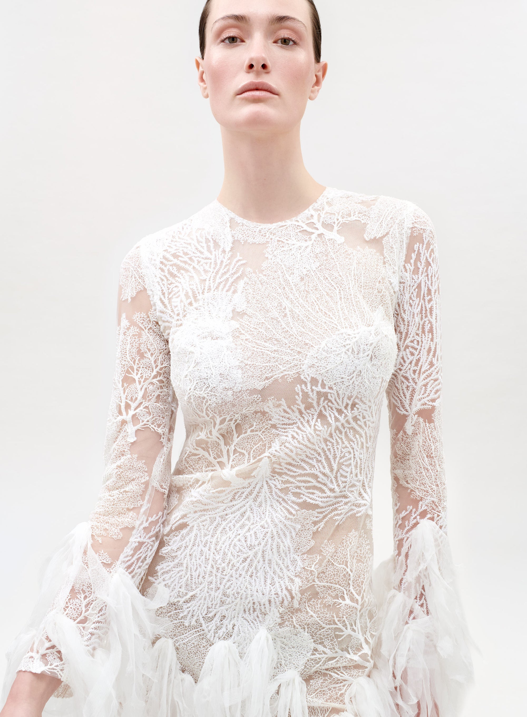Woman wearing a white lace dress against a plain background