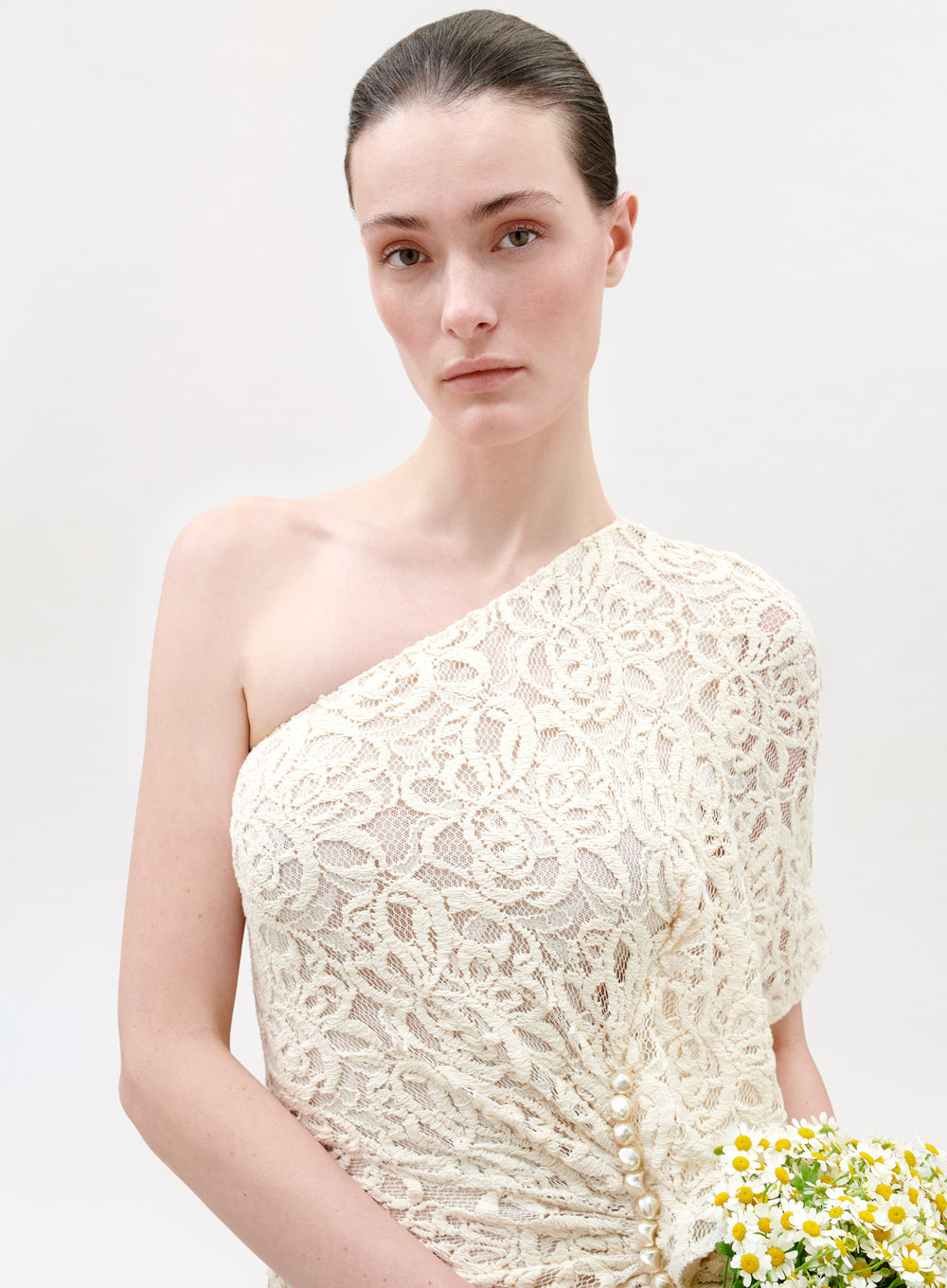 Woman wearing a white lace one-shoulder dress against a light background