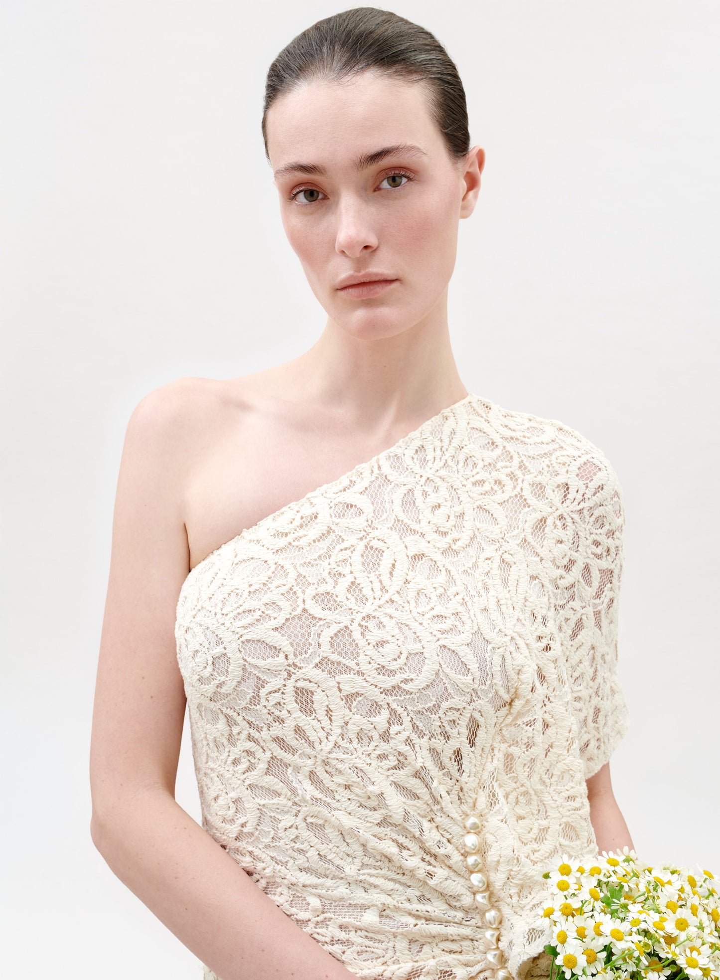 Woman wearing a white lace one-shoulder dress against a light background