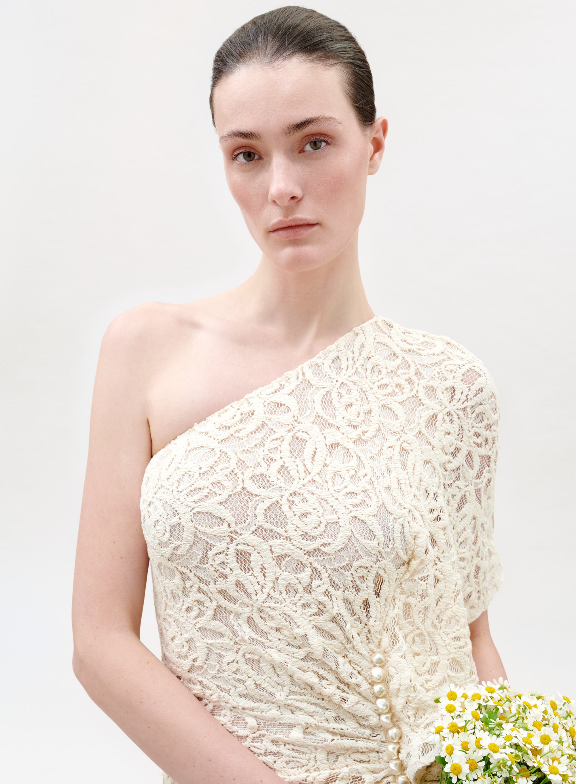 Woman wearing a white lace one-shoulder dress against a light background