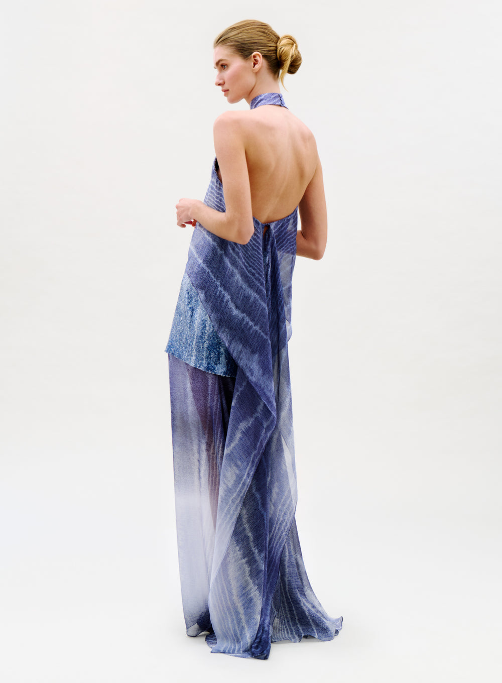 Woman in the Amalia Skirt, a flowing blue and purple semi-sheer Italian skirt, stands against a plain light background, looking to the side with her hair in a neat bun.