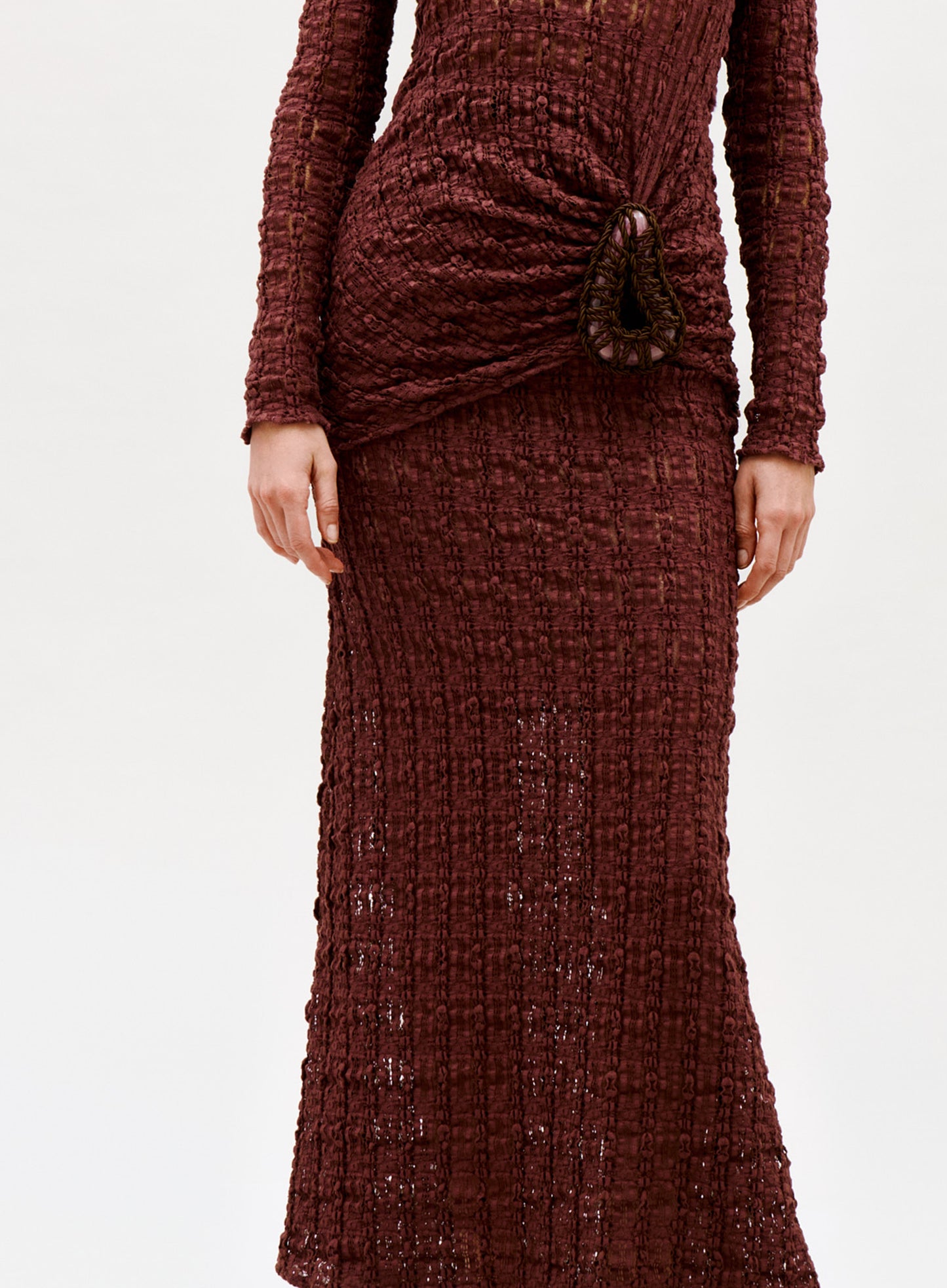 A person wearing the Ciji Skirt, a textured burgundy knit piece with a distinctive gathered hip detail and long sleeves. The photo shows the body from shoulders down against a plain light background.