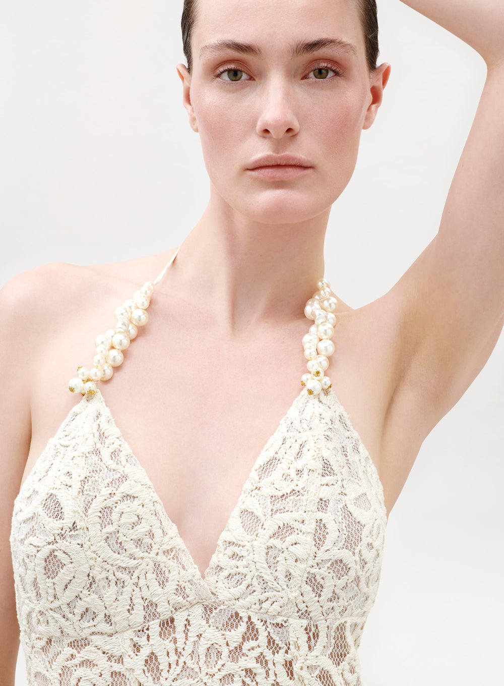 Woman wearing a white lace dress with pearl straps against a plain background