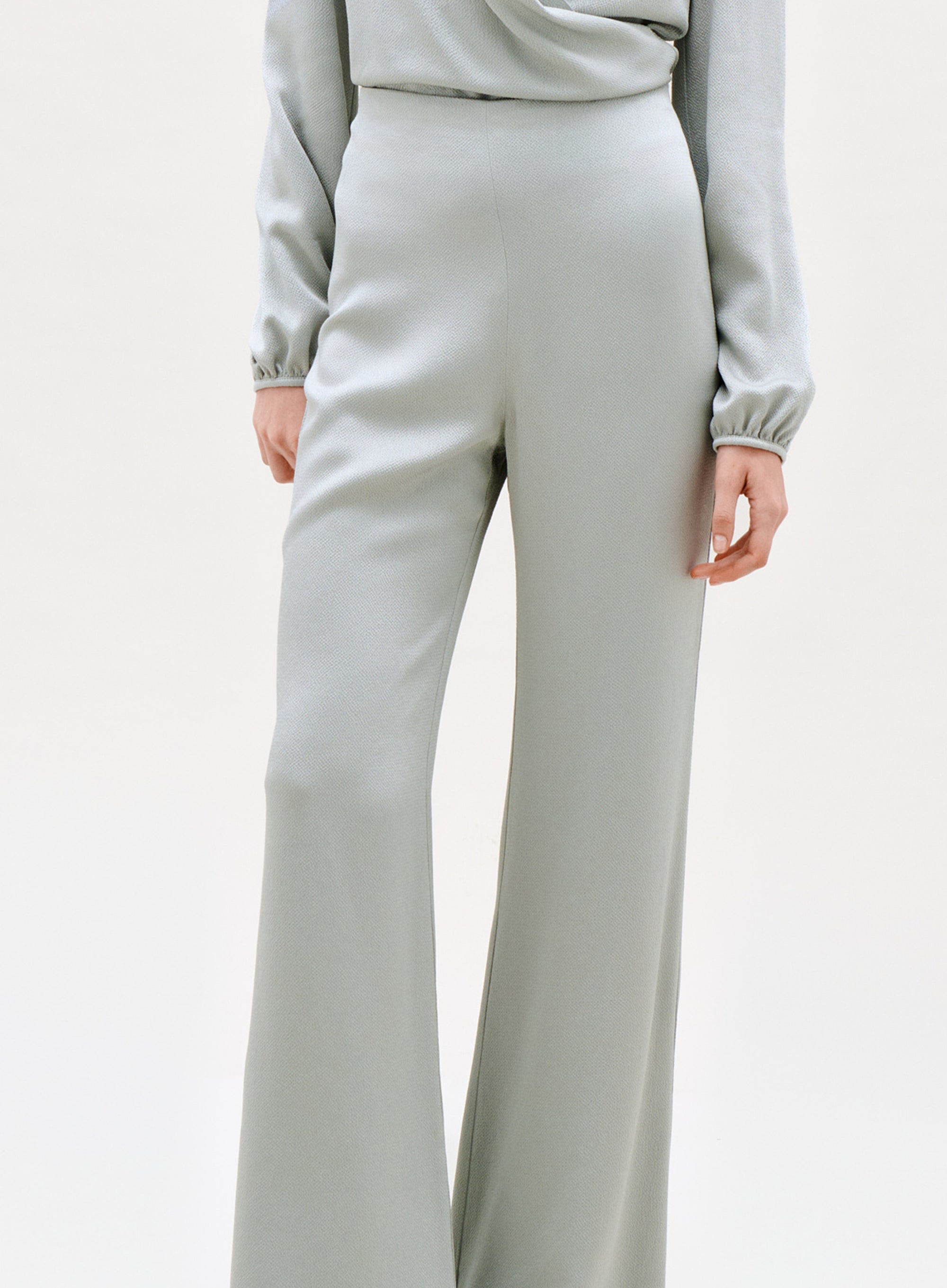 A person wearing the Palermo Pant—high-waisted, light gray wide-leg pants—shown from mid-torso to feet with one hand by their side against a plain background.