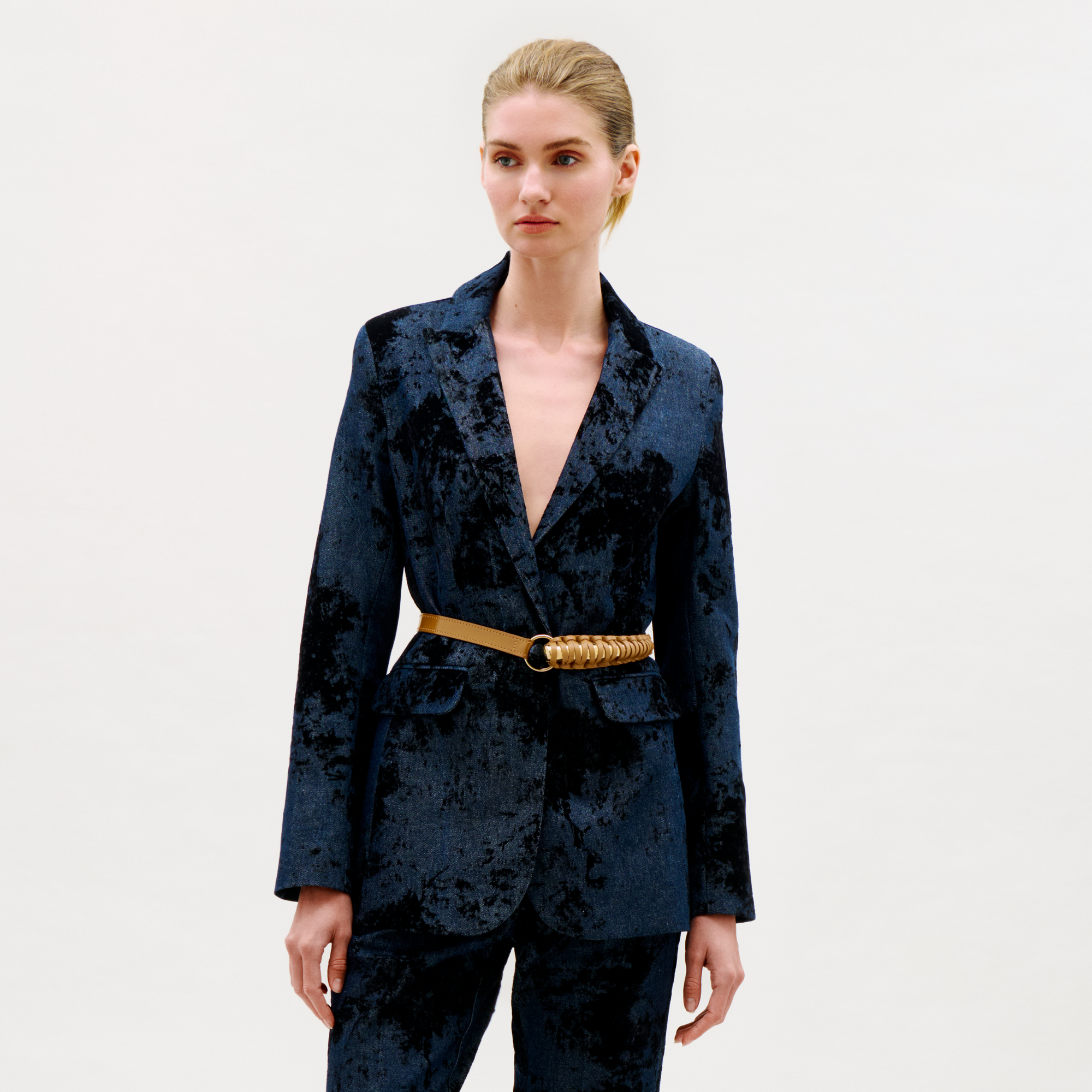Woman wearing a blue velvet suit with a gold belt on a white background