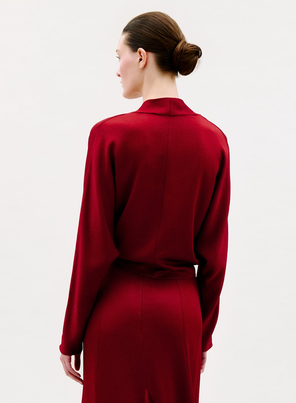 A woman with brown hair in a neat bun is seen from behind, wearing the Reiko Blouse against a plain white background.