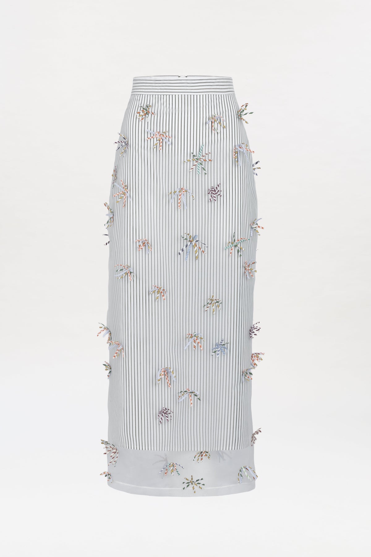 Uma Skirt: A long, high-waisted white skirt featuring thin vertical black stripes and colorful small 3D floral embellishments scattered across the fabric.