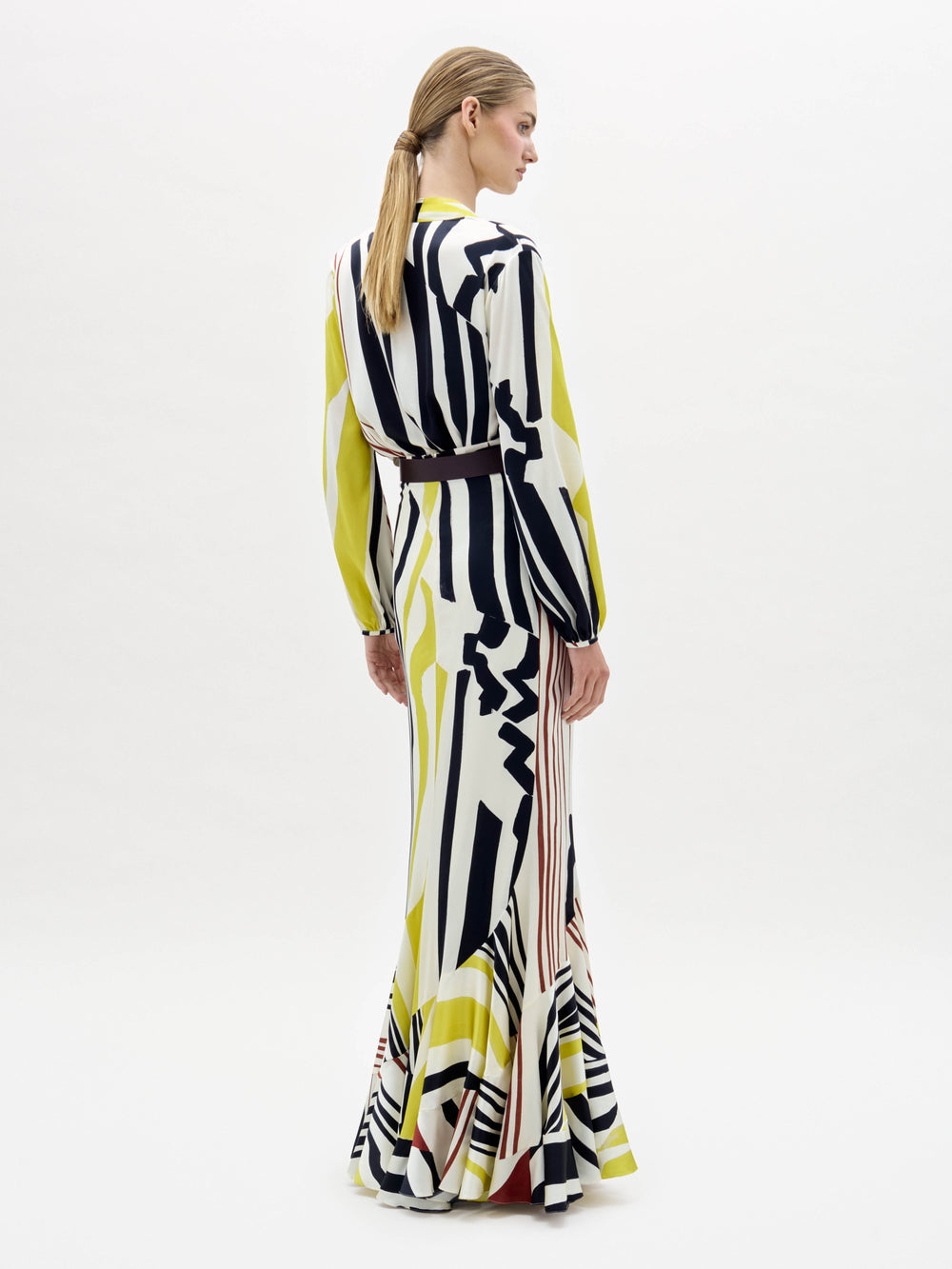 A woman stands wearing the Florina Skirt, a long, flowing piece with vertical and diagonal stripes in black, yellow, and red.