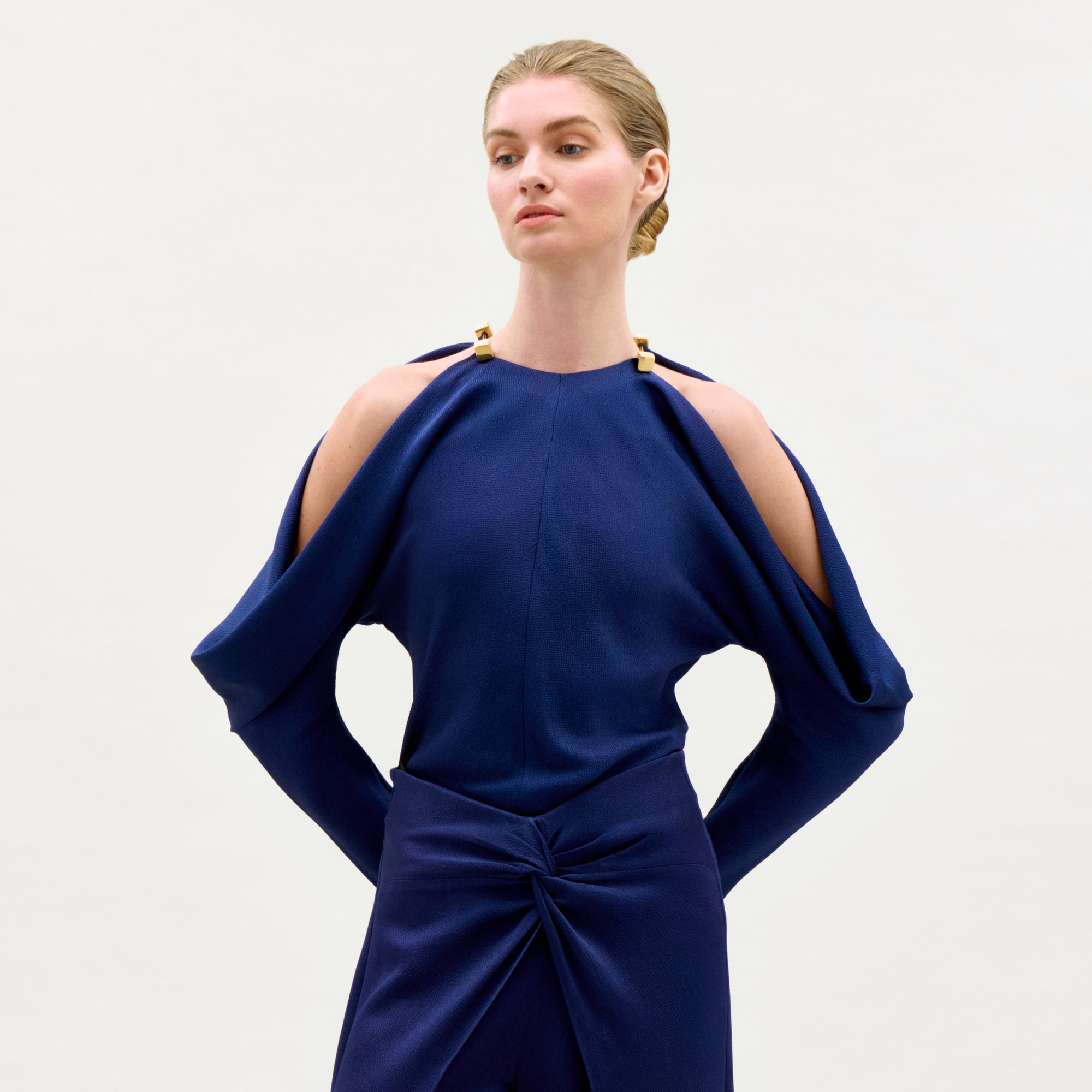 Woman wearing a blue dress with cut-out shoulders on a light gray background