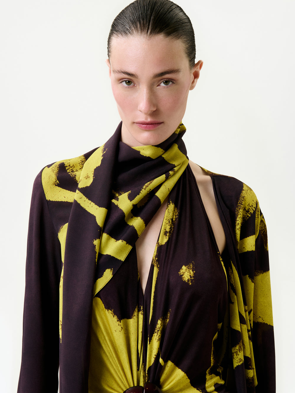 A person with slicked-back hair wears the Luisanna Cape, crafted from luxurious Italian fabric with bold yellow patterns, draped stylishly over the shoulders and chest against a plain white background.