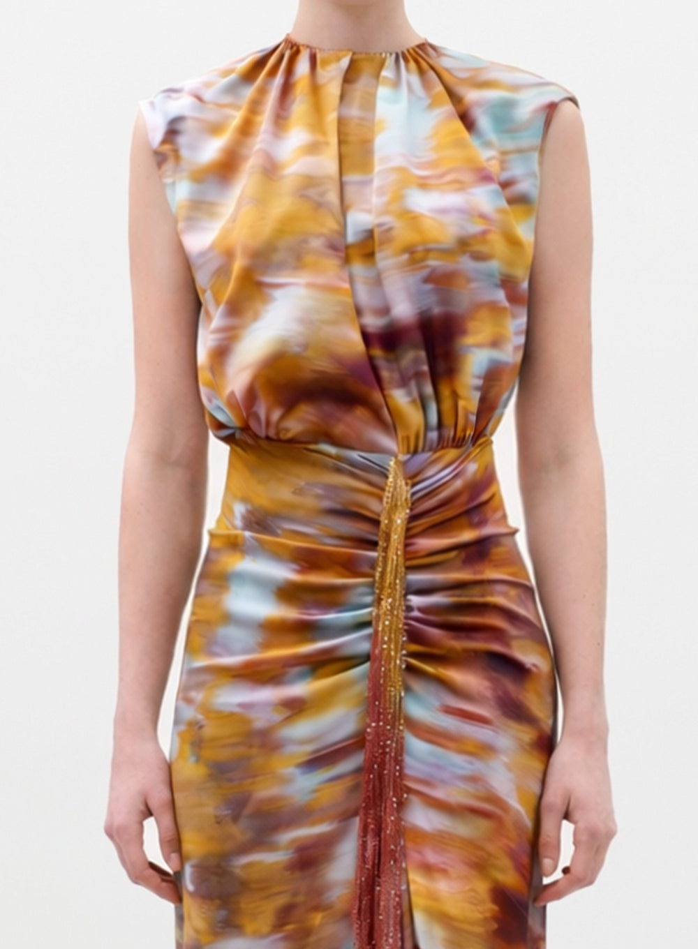A person wearing the Winona Dress—a sleeveless style with a colorful abstract pattern in yellow, orange, brown, blue, and white—featuring pleats, a gathered waist, and beaded fringe down the front.
