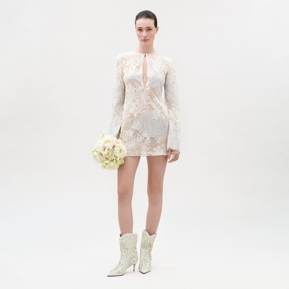 Woman wearing a white lace dress and matching boots on a plain background