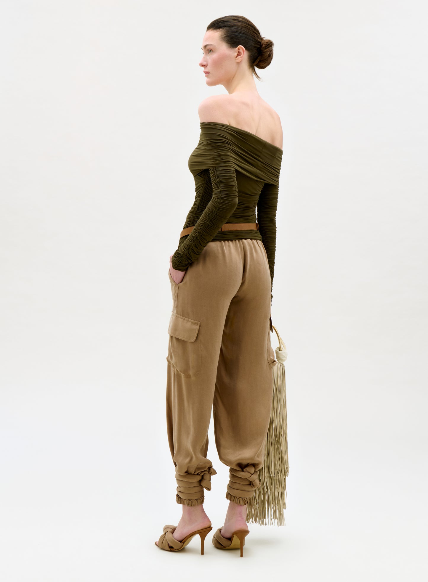 Woman wearing an off-shoulder green top and beige fringed pants on a white background