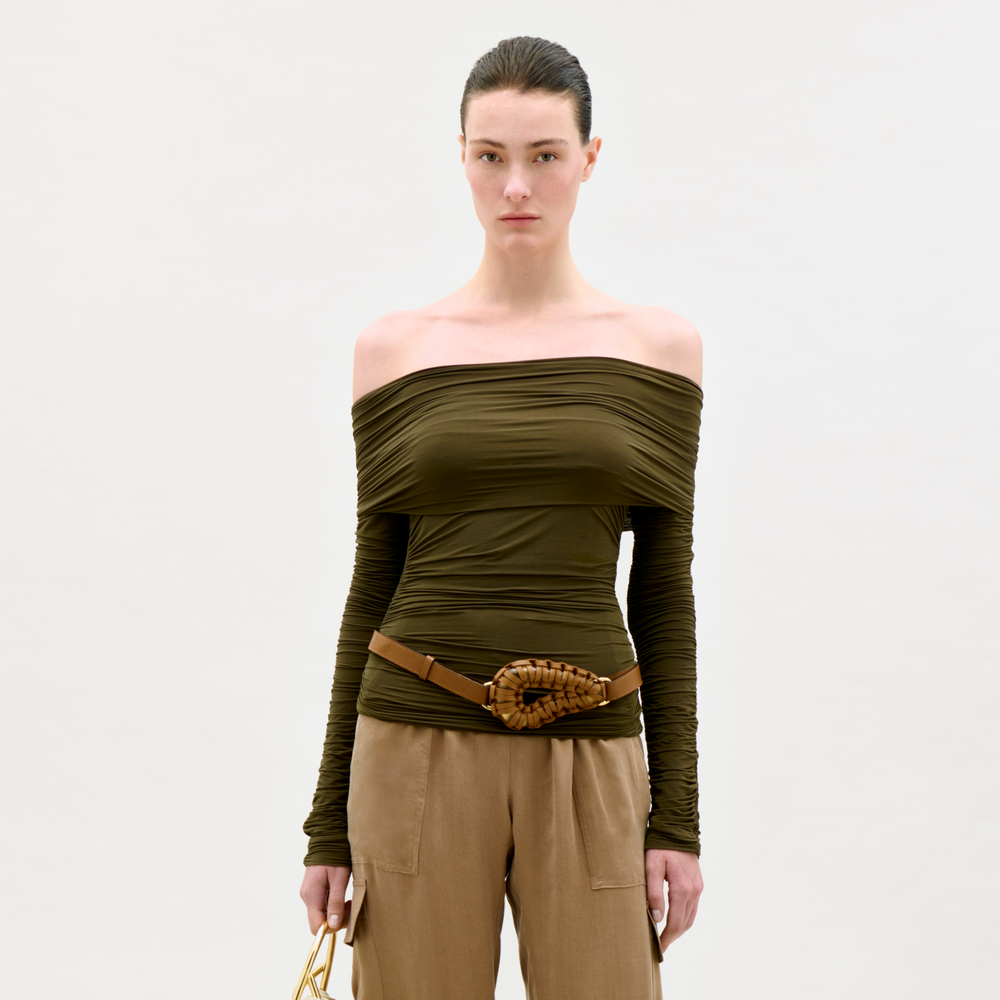 Woman wearing an off-shoulder green top and beige pants on a white background