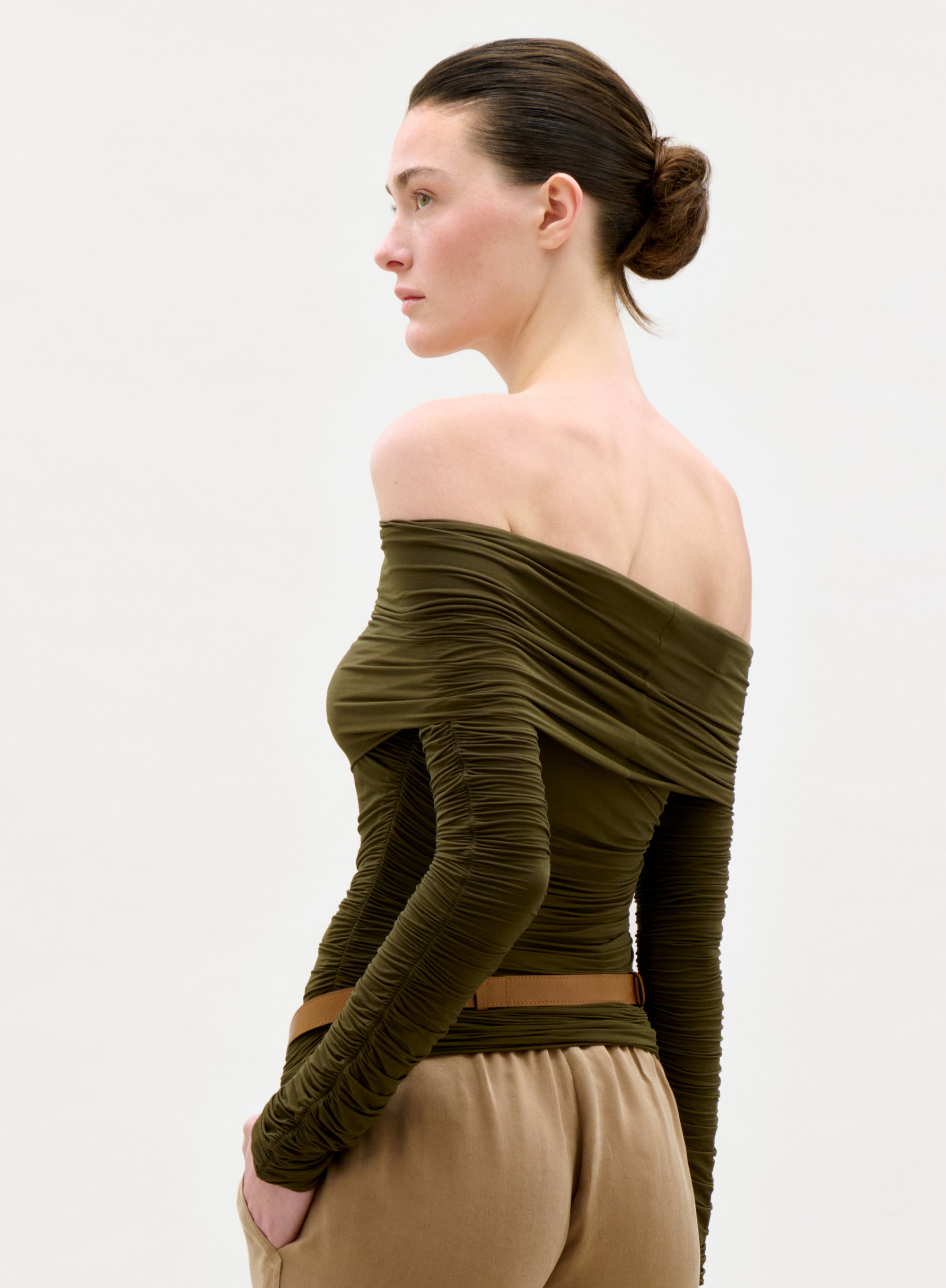 Woman wearing an off-shoulder green top and beige pants on a white background