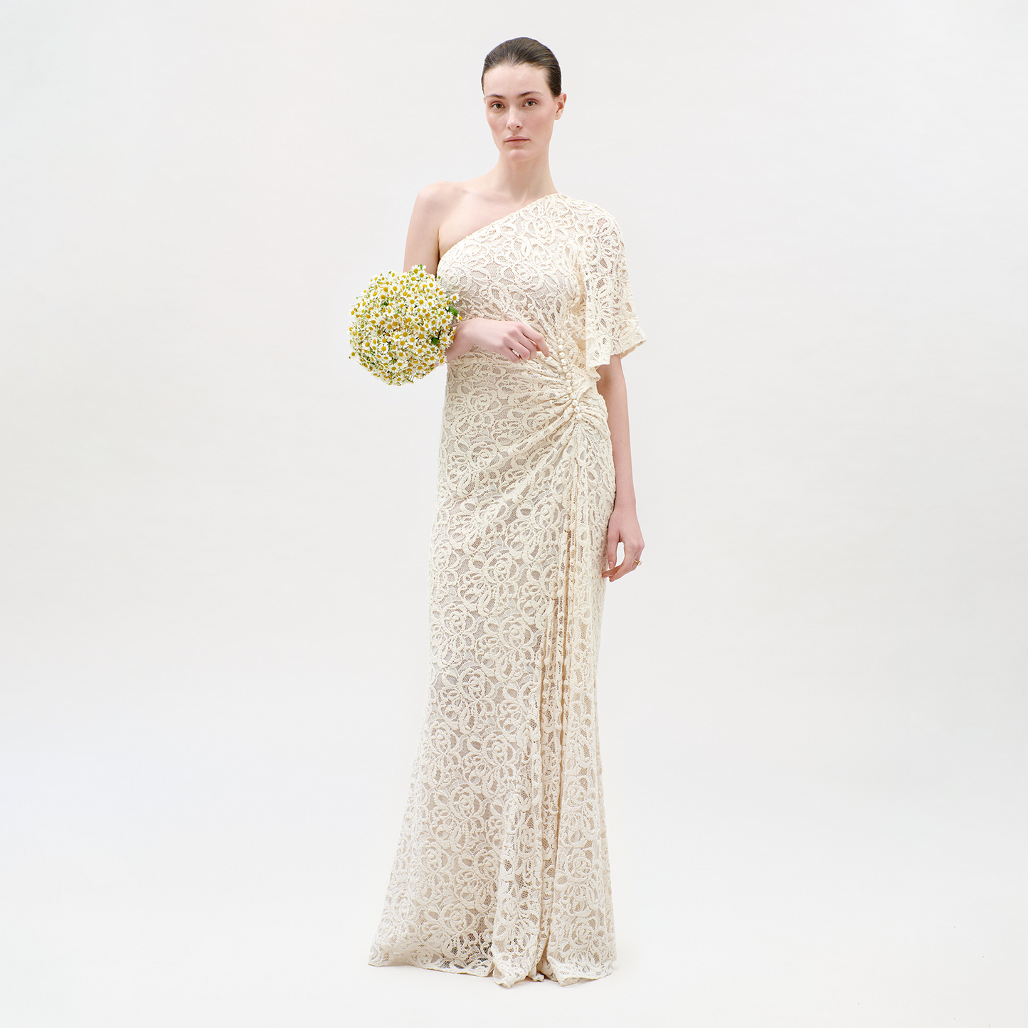 Woman in a long, light-colored lace dress holding a bouquet on a white background