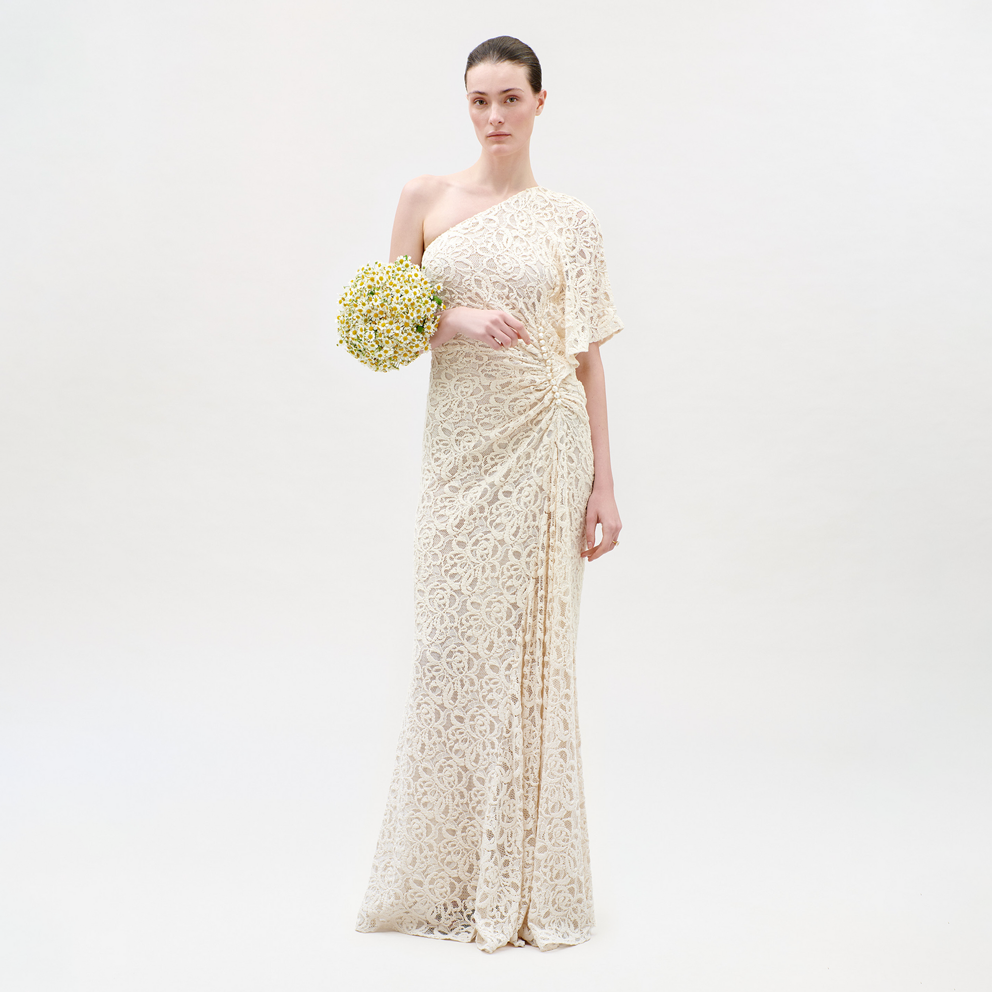 Woman in a long, light-colored lace dress holding a bouquet on a white background