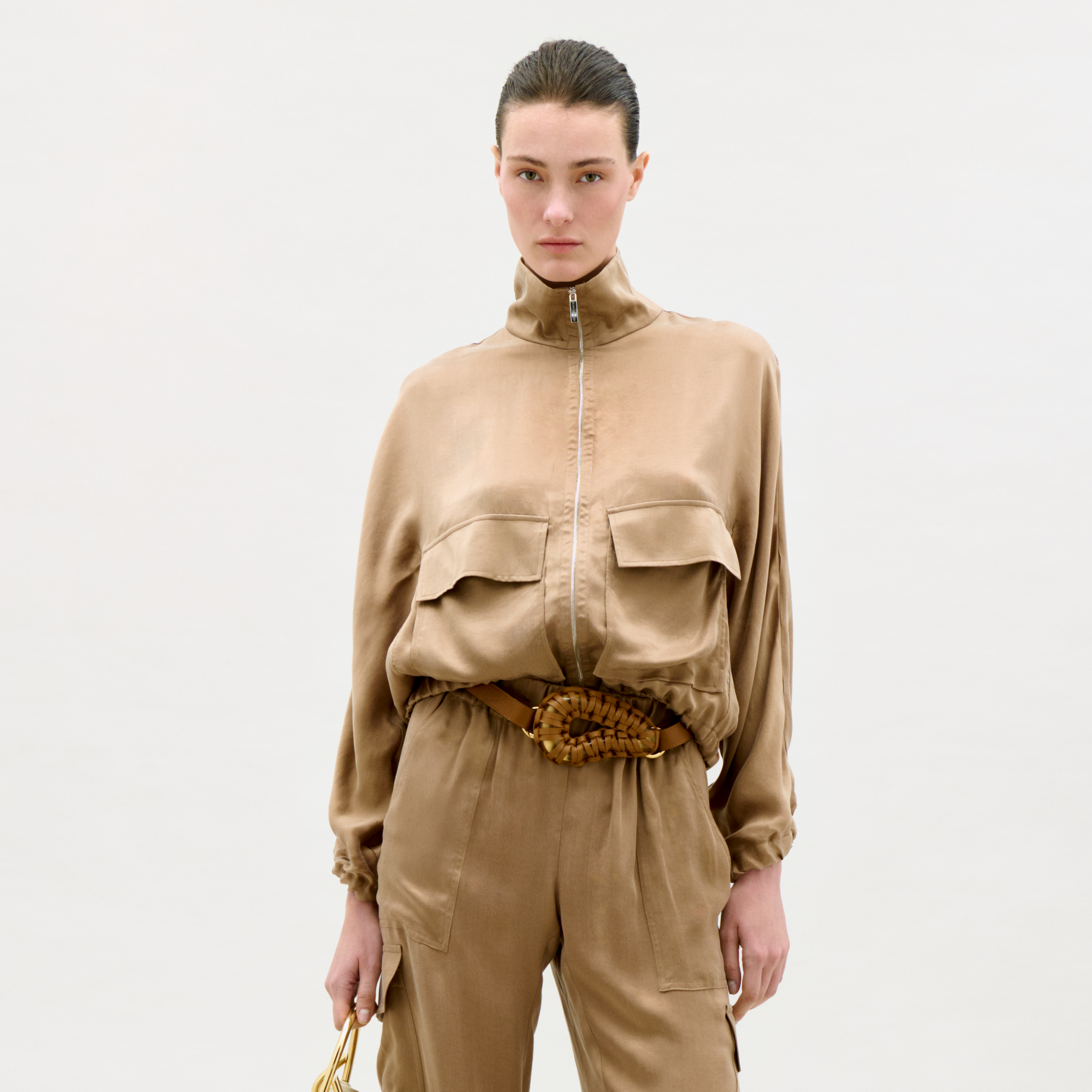 Person wearing a beige outfit with a belt on a white background