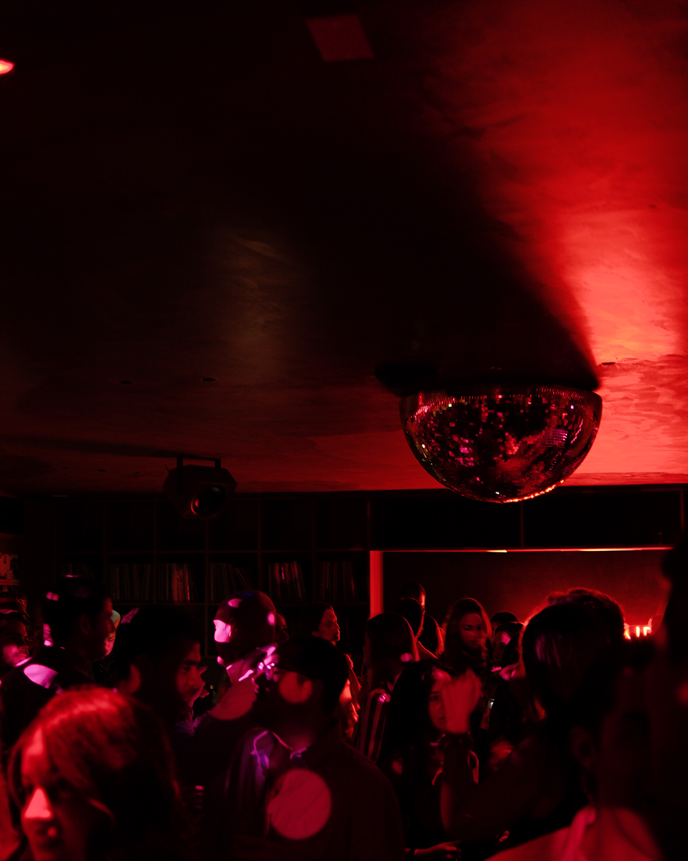 Red-lit nightclub scene with people and a disco ball.