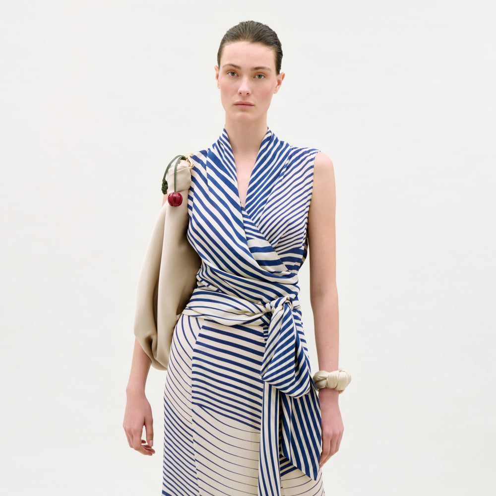Woman wearing a blue and white striped dress with a beige bag on a light gray background