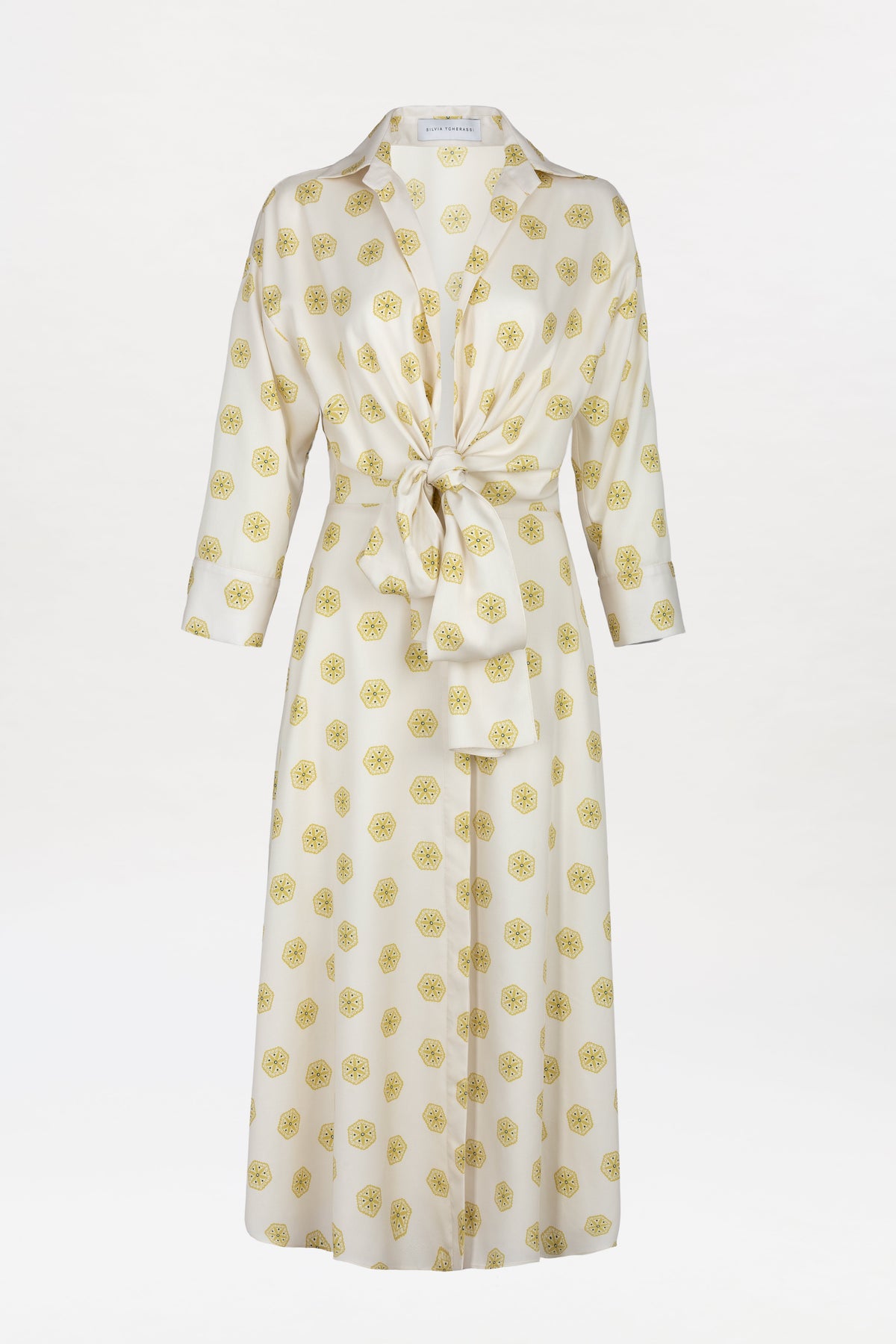 The Milene Blouse is a long-sleeved, white button-down top featuring a front knot at the waist and a yellow circular pattern throughout, displayed on a plain white background.