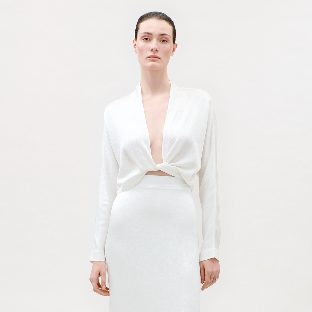 Woman wearing a white long-sleeve top and skirt set on a plain background