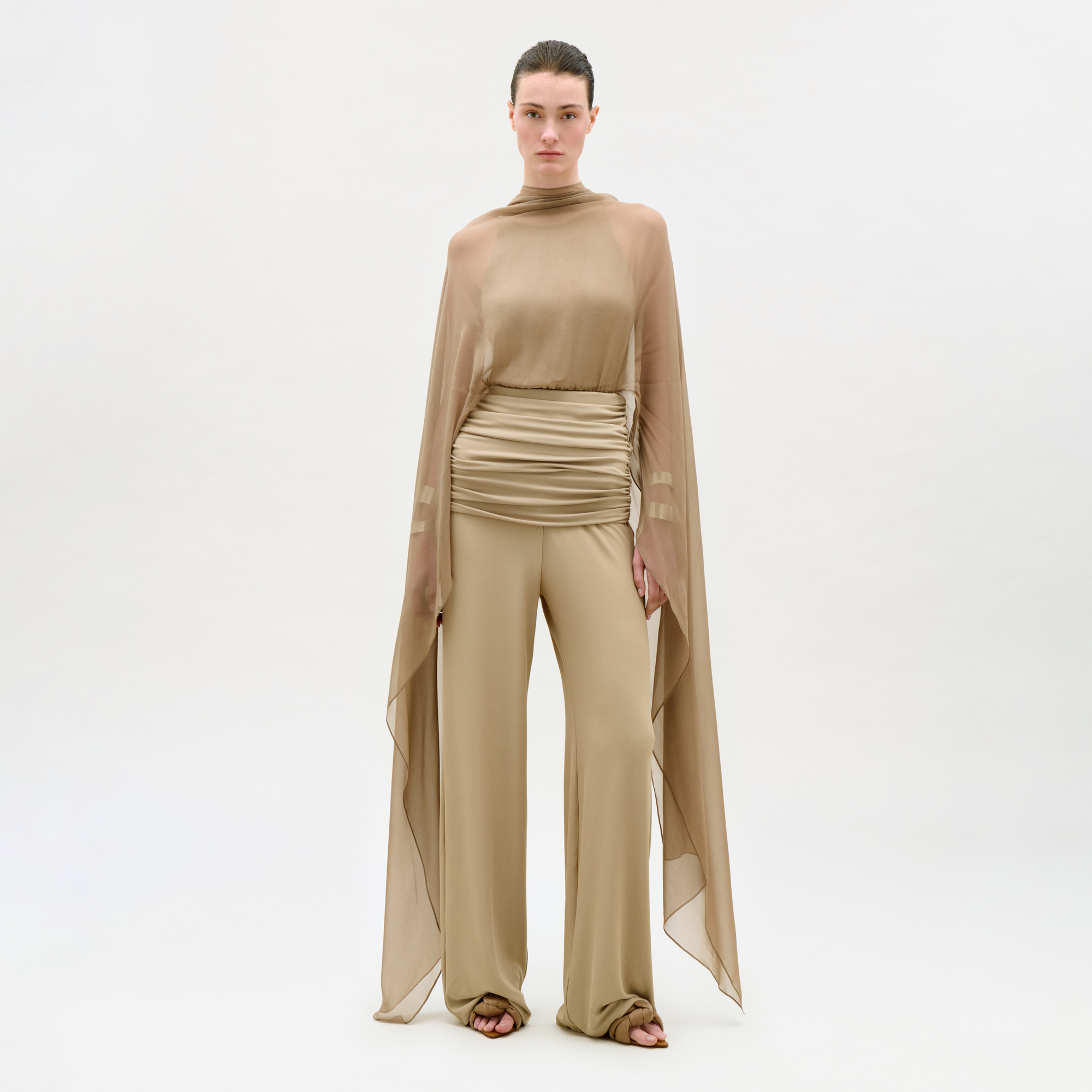 Woman wearing a beige outfit with a cape on a white background