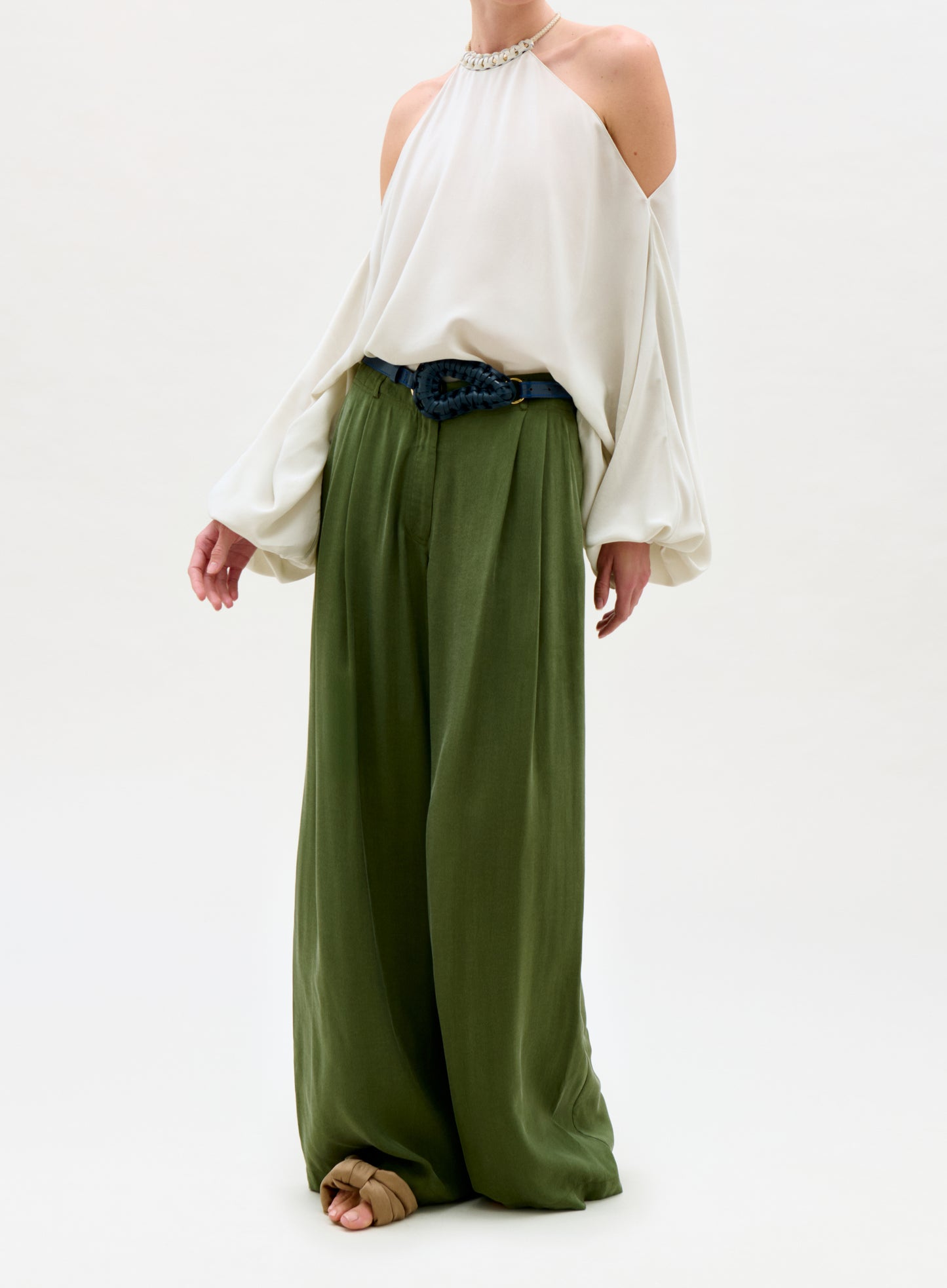Person wearing a white off-shoulder top and green wide-leg pants on a white background