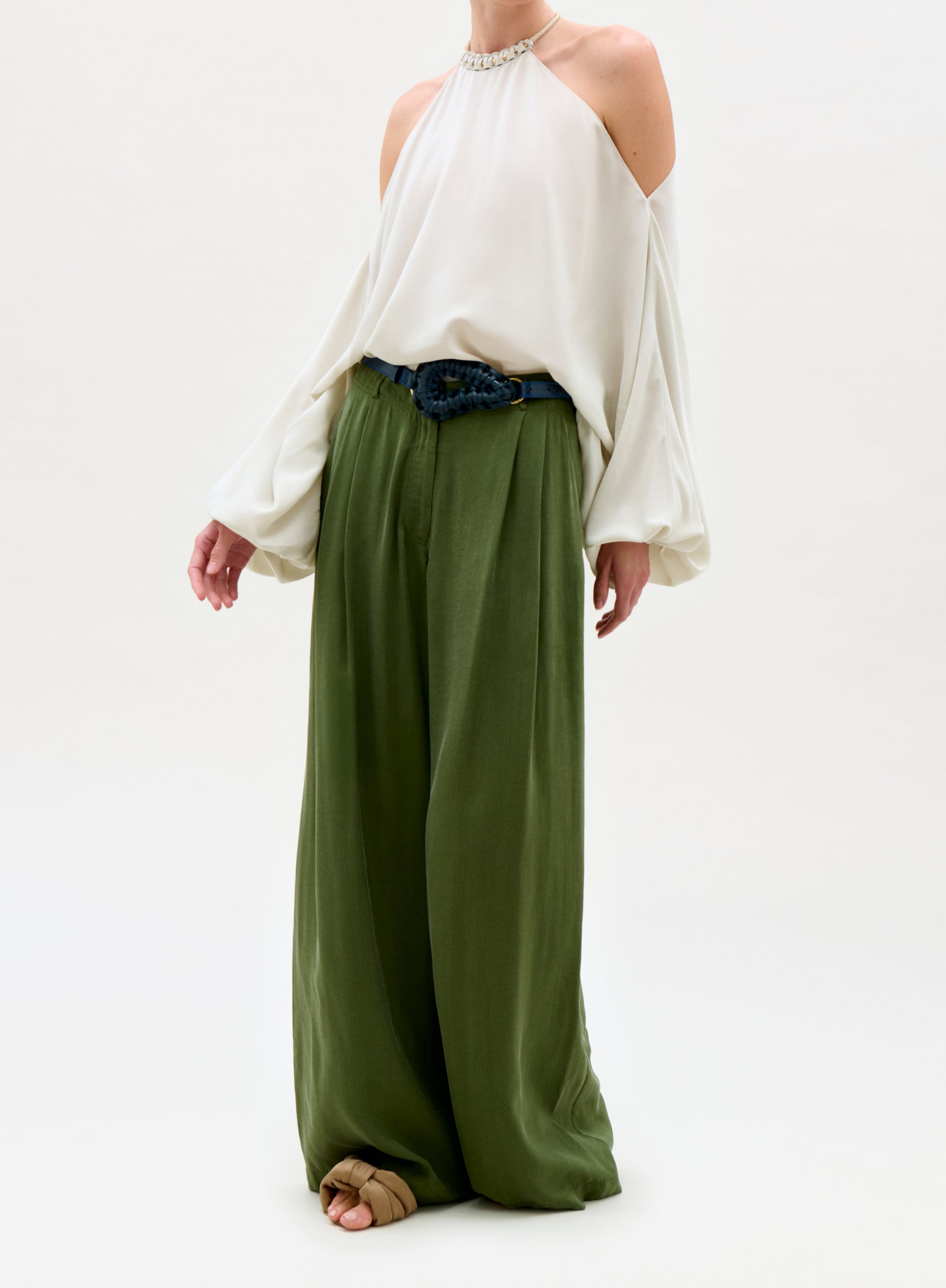 Person wearing a white off-shoulder top and green wide-leg pants on a white background
