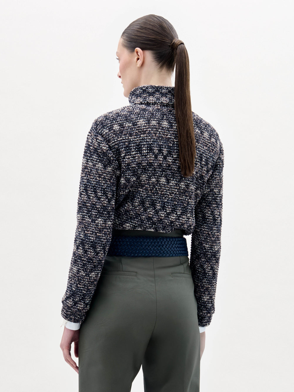 A person stands against a plain background wearing the Zalta Jacket, olive green pants, and a wide blue belt with a large gold buckle.