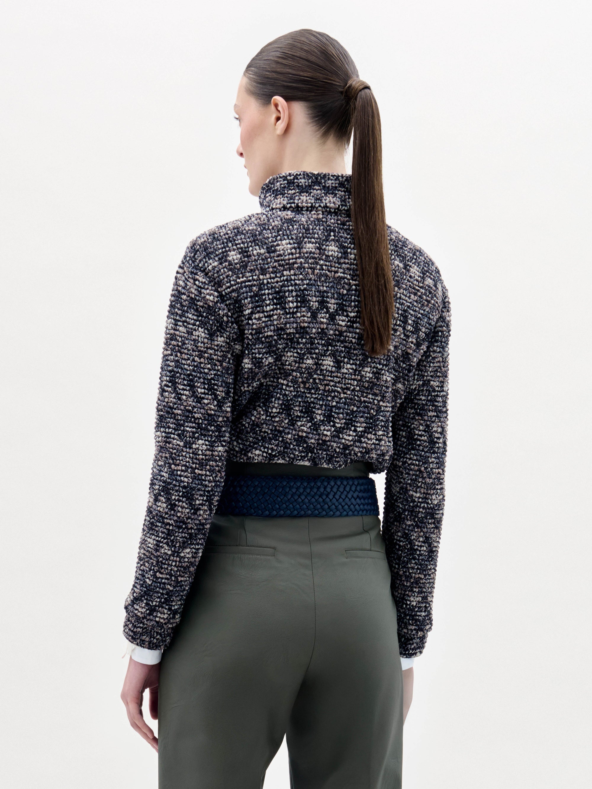 A person stands against a plain background wearing the Zalta Jacket, olive green pants, and a wide blue belt with a large gold buckle.