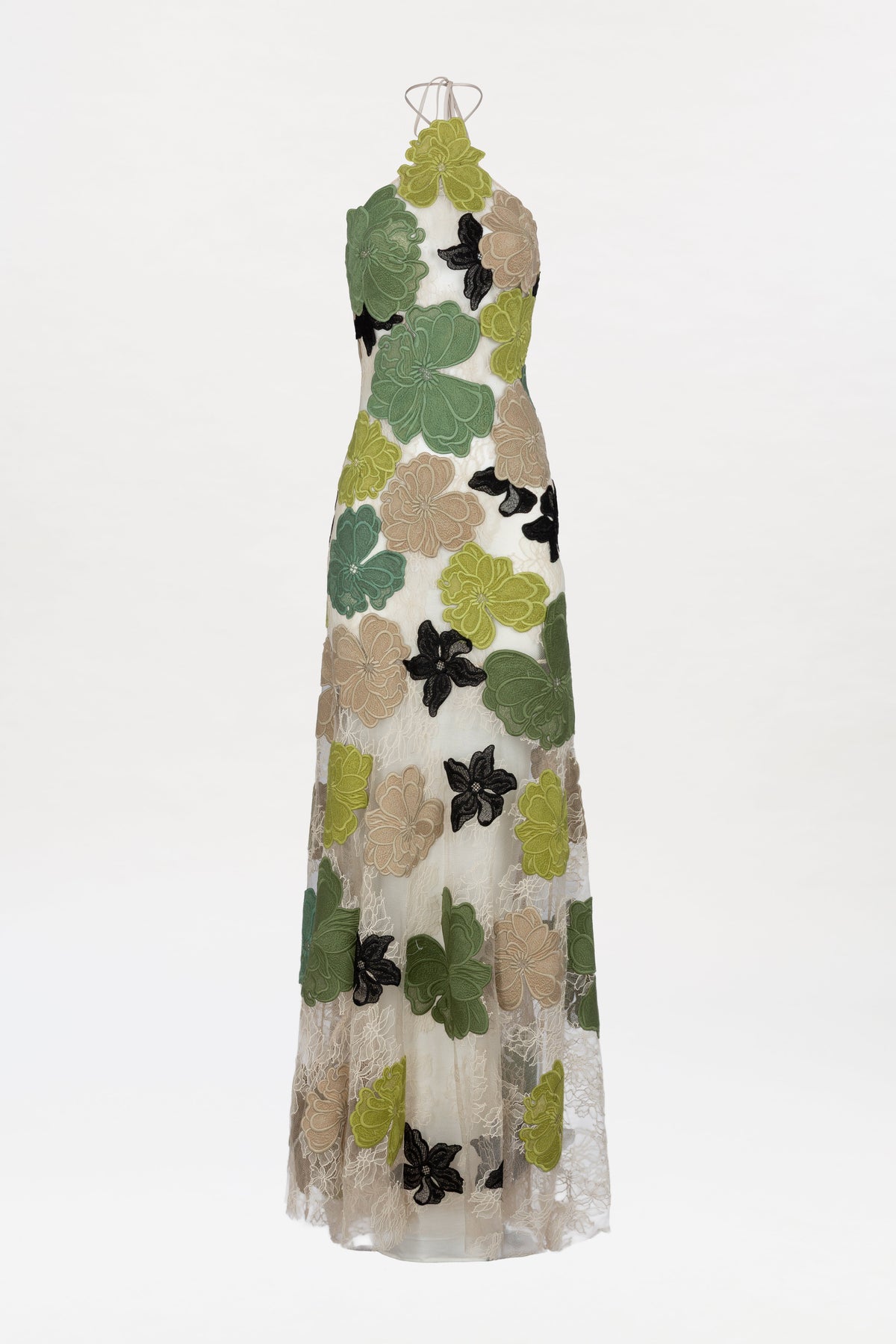 The Xenia Dress is a sleeveless, floor-length white lace dress adorned with bold green, beige, and black floral appliqués, showcased on a mannequin against a white background.