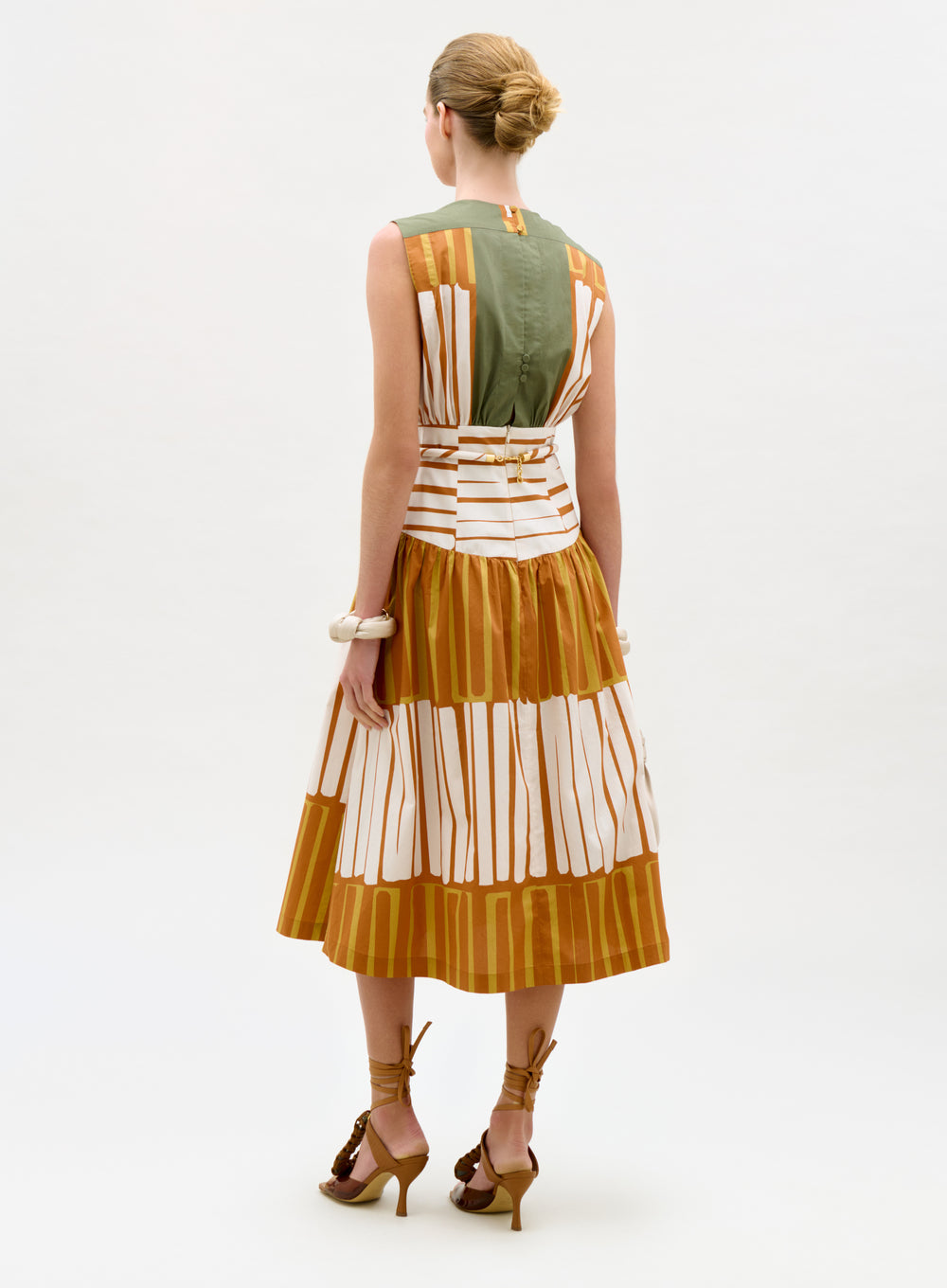 Woman wearing a sleeveless dress with vertical stripes in green, orange, and white on a white background