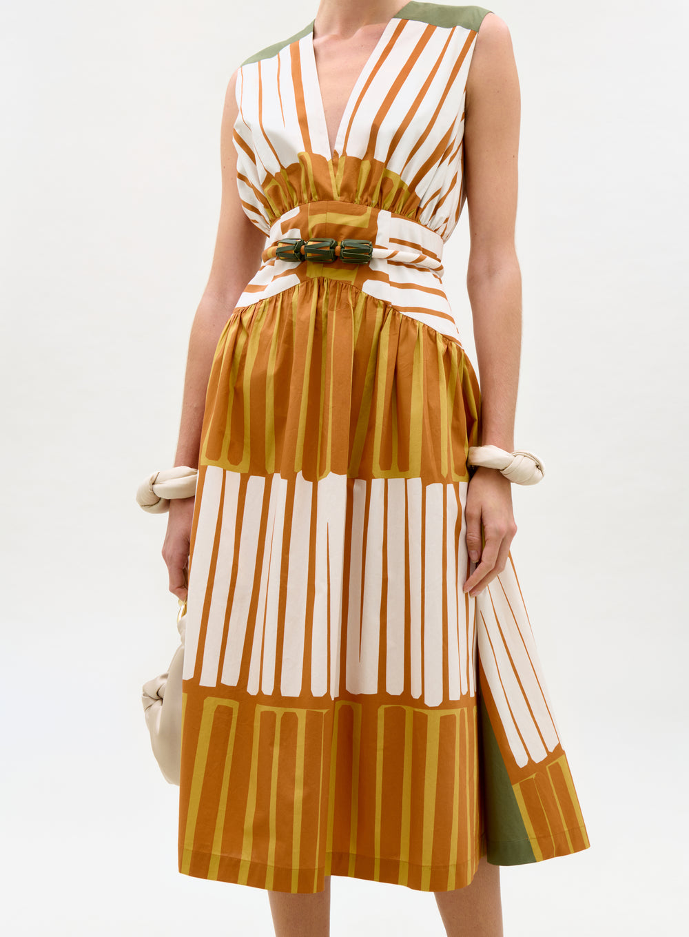 Woman wearing a sleeveless dress with vertical stripes in brown, white, and green on a white background