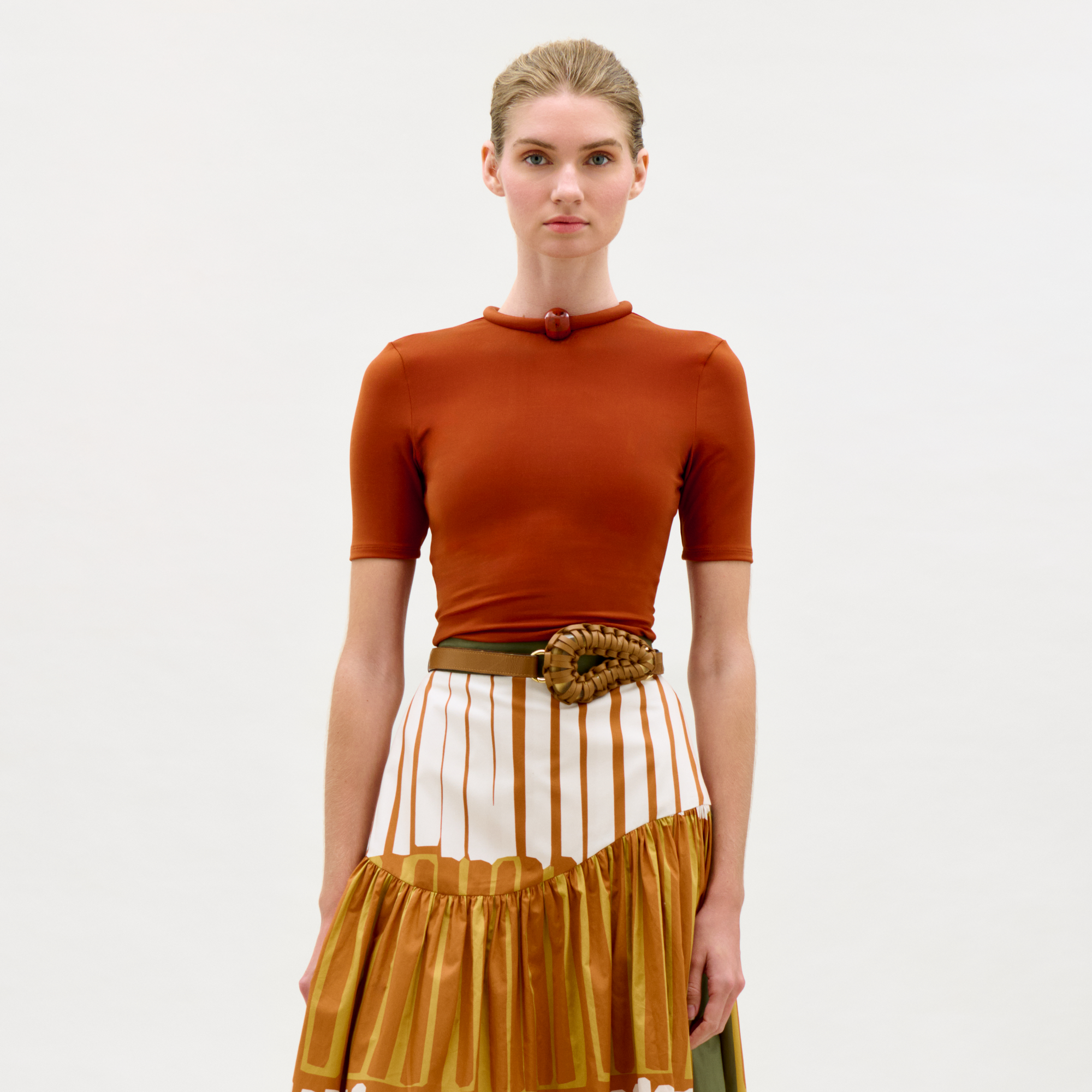 Woman wearing a rust-colored top and mustard yellow skirt with a white background